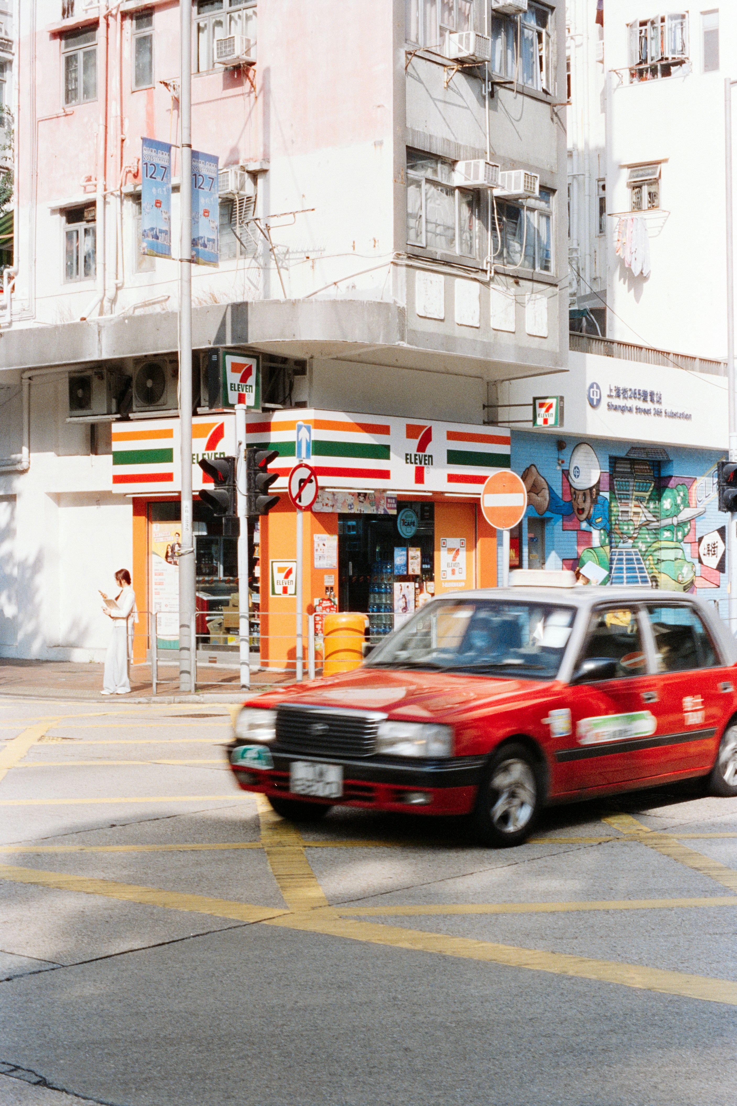 Red taxi drives past a 7-eleven store.