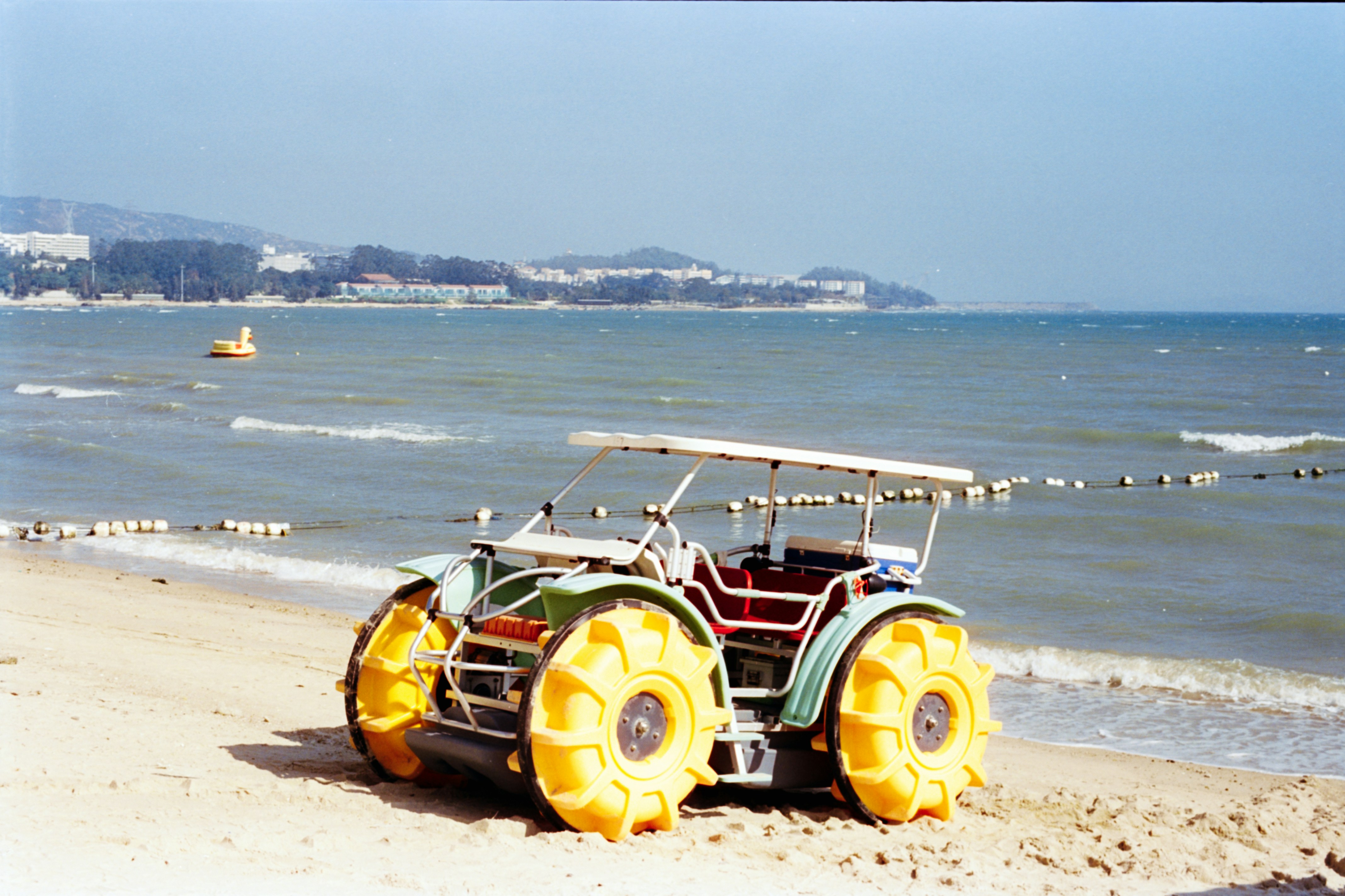 Amphibious vehicle with large yellow wheels on sandy beach.