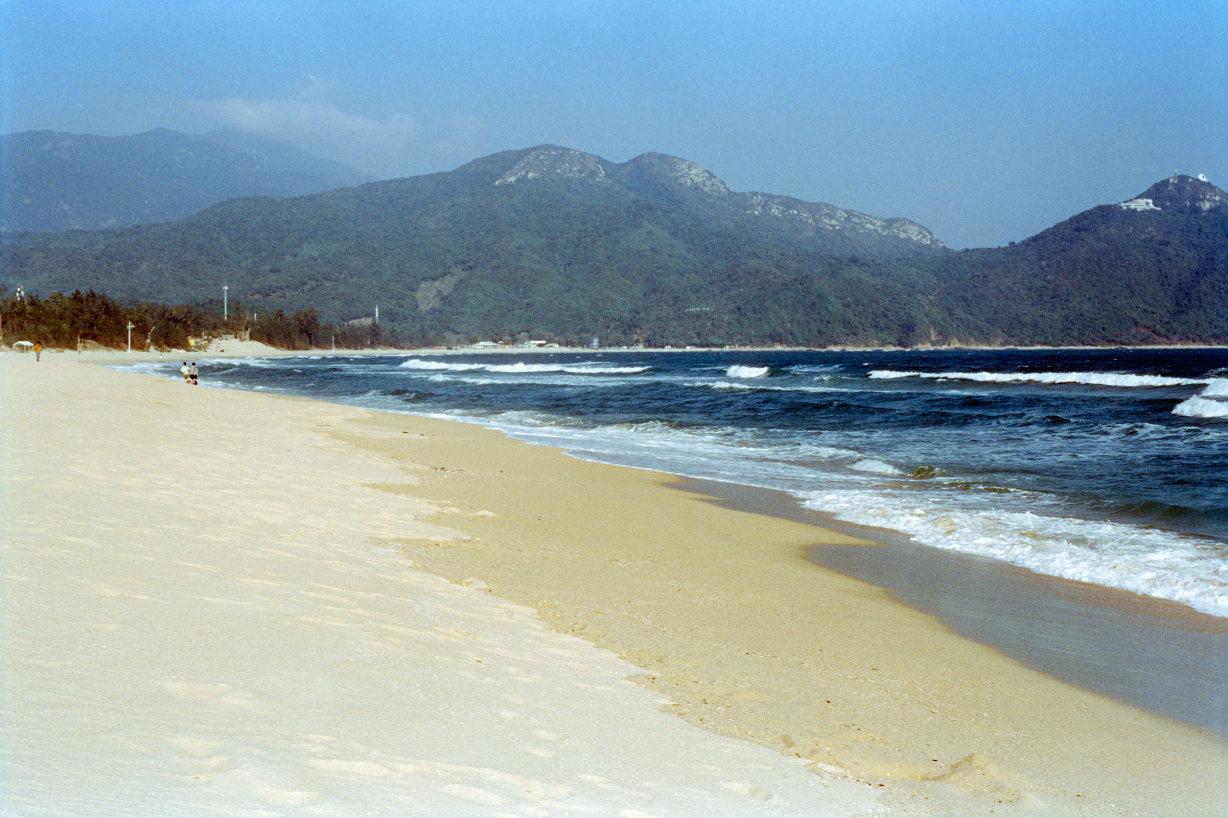 Sandy beach with blue ocean waves and mountains.