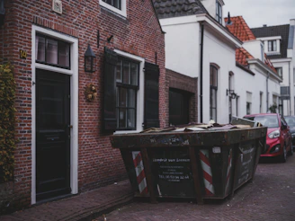 A large dumpster sits on a street next to buildings.