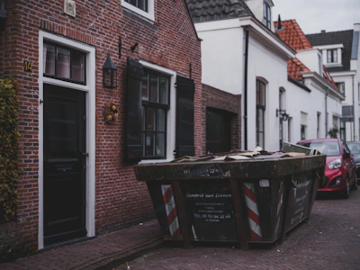 A large dumpster sits on a street next to buildings.