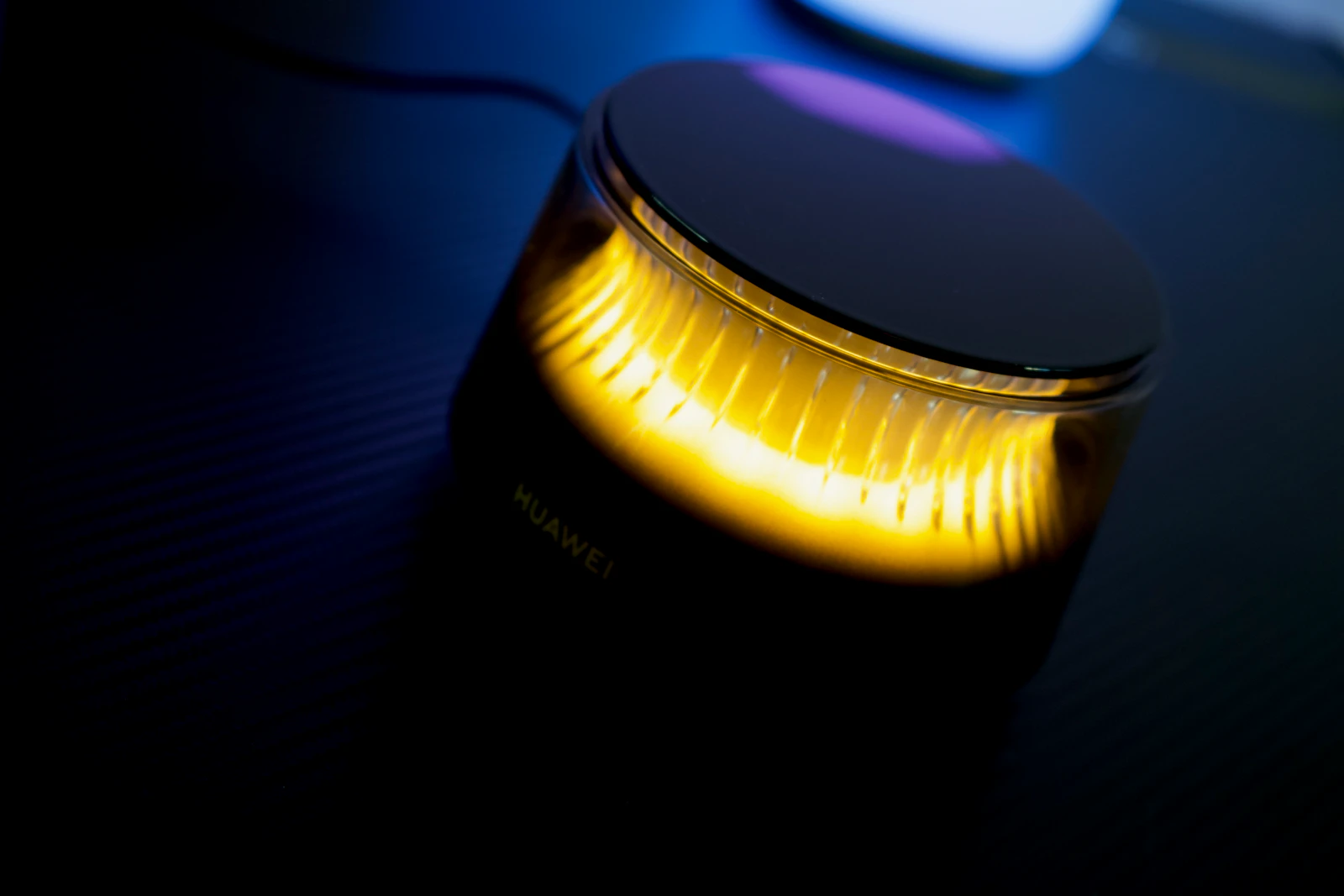 Cylindrical Huawei mesh Wi-Fi router glowing warm yellow on a dark desk, with a power cable attached