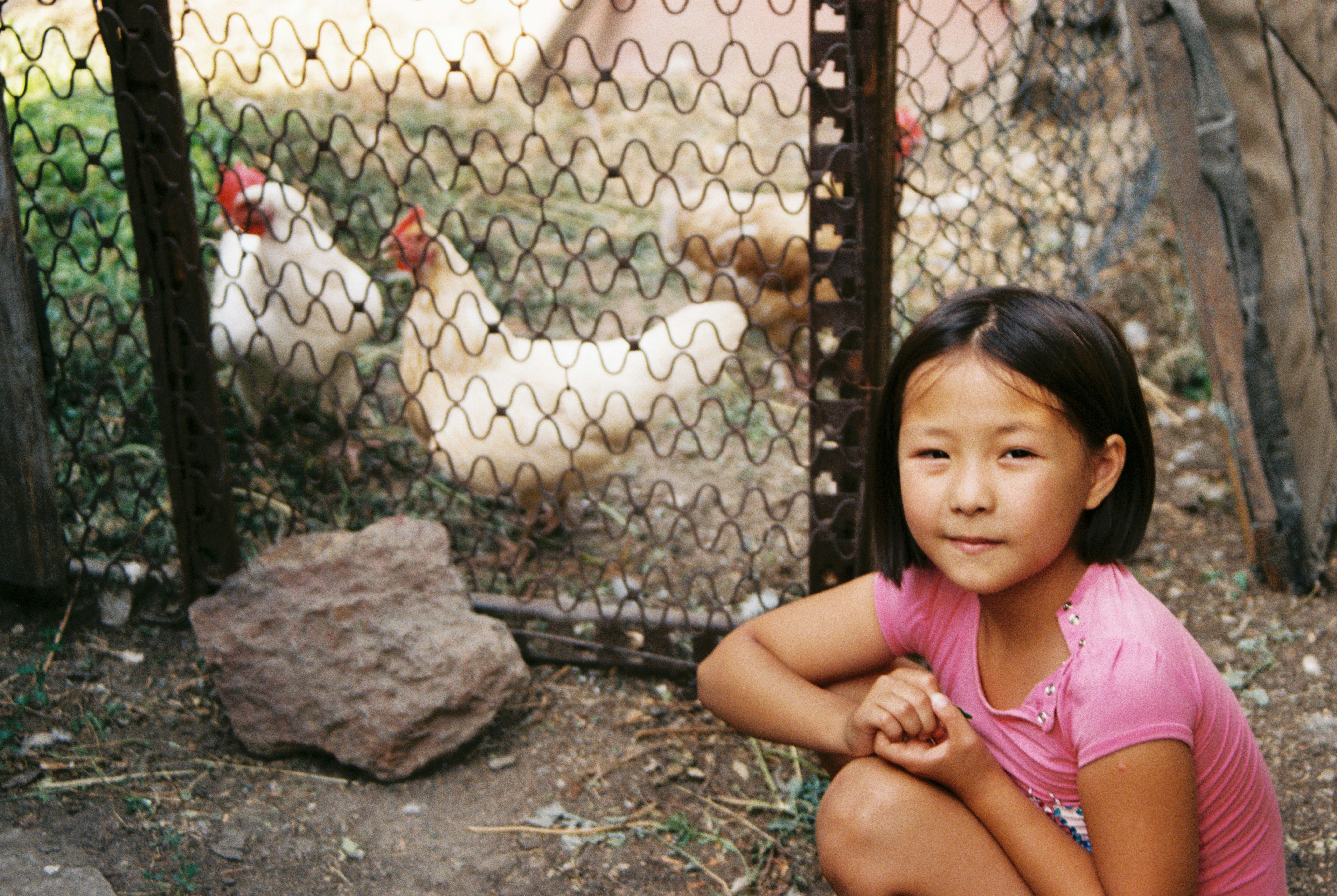 A young girl poses near chickens in a coop. (Photo by DIANA HAUAN on Unsplash)