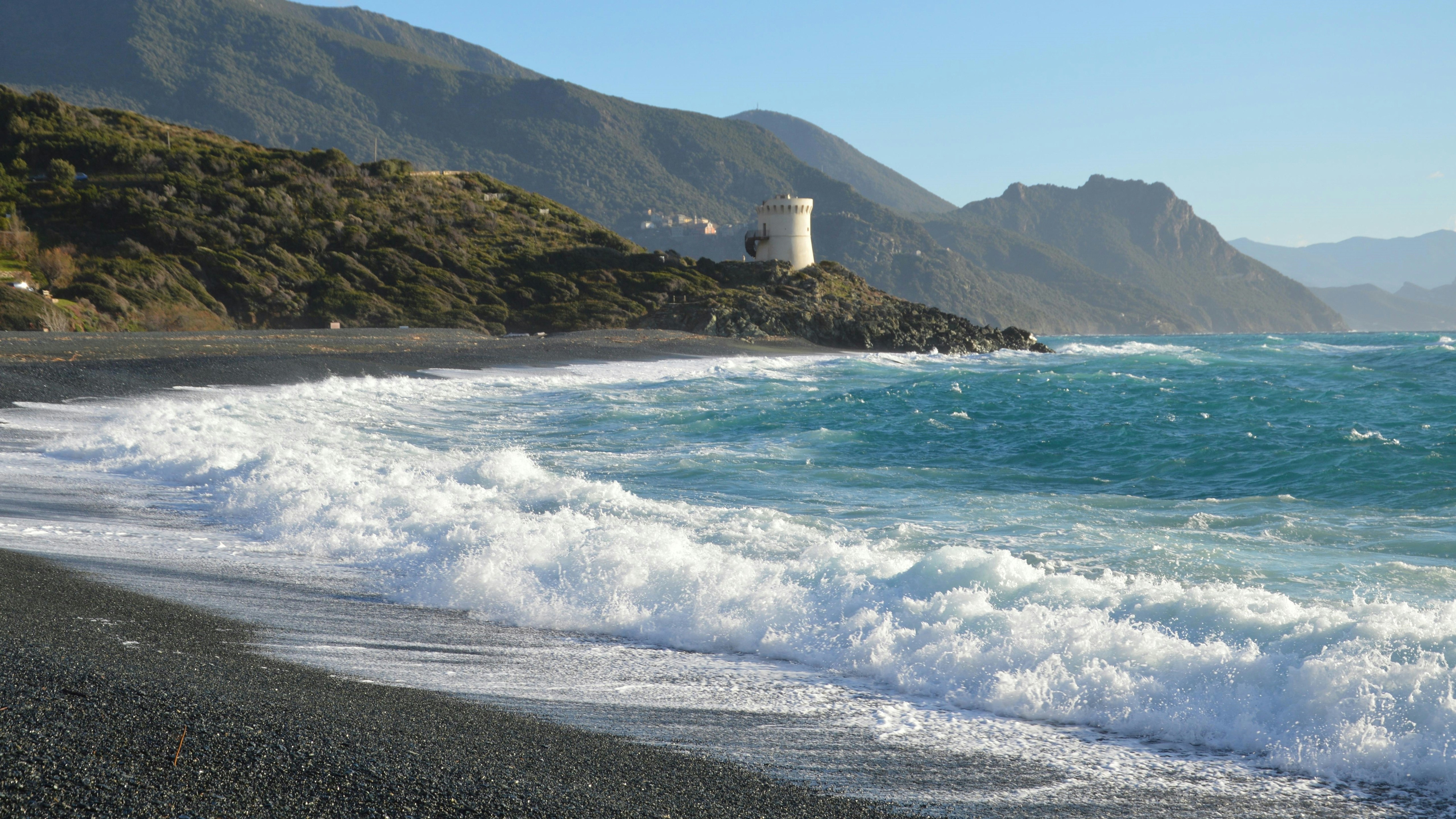 Waves crash on a rocky beach with a tower.