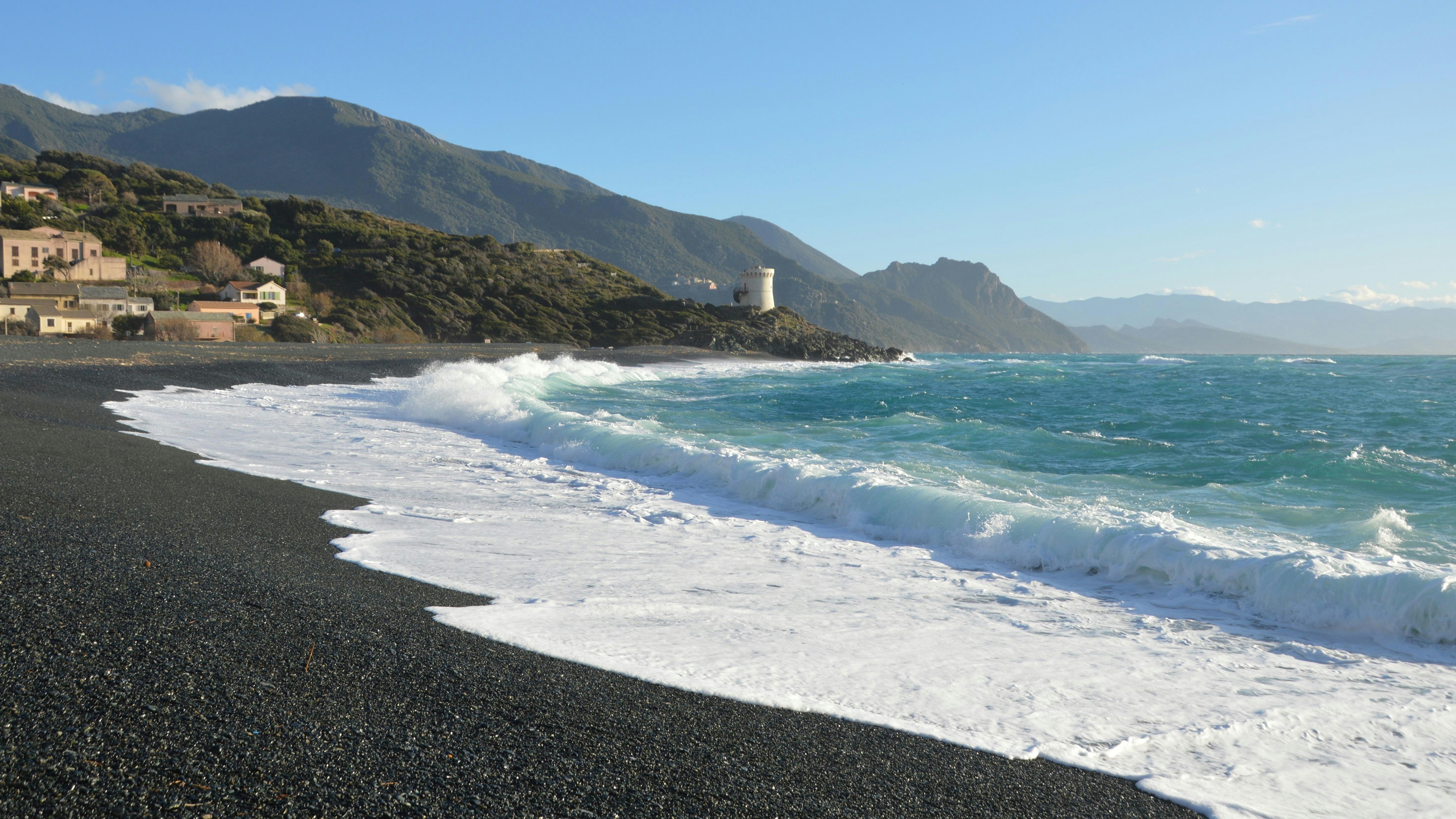 Waves crash on a rocky beach with a lighthouse.
