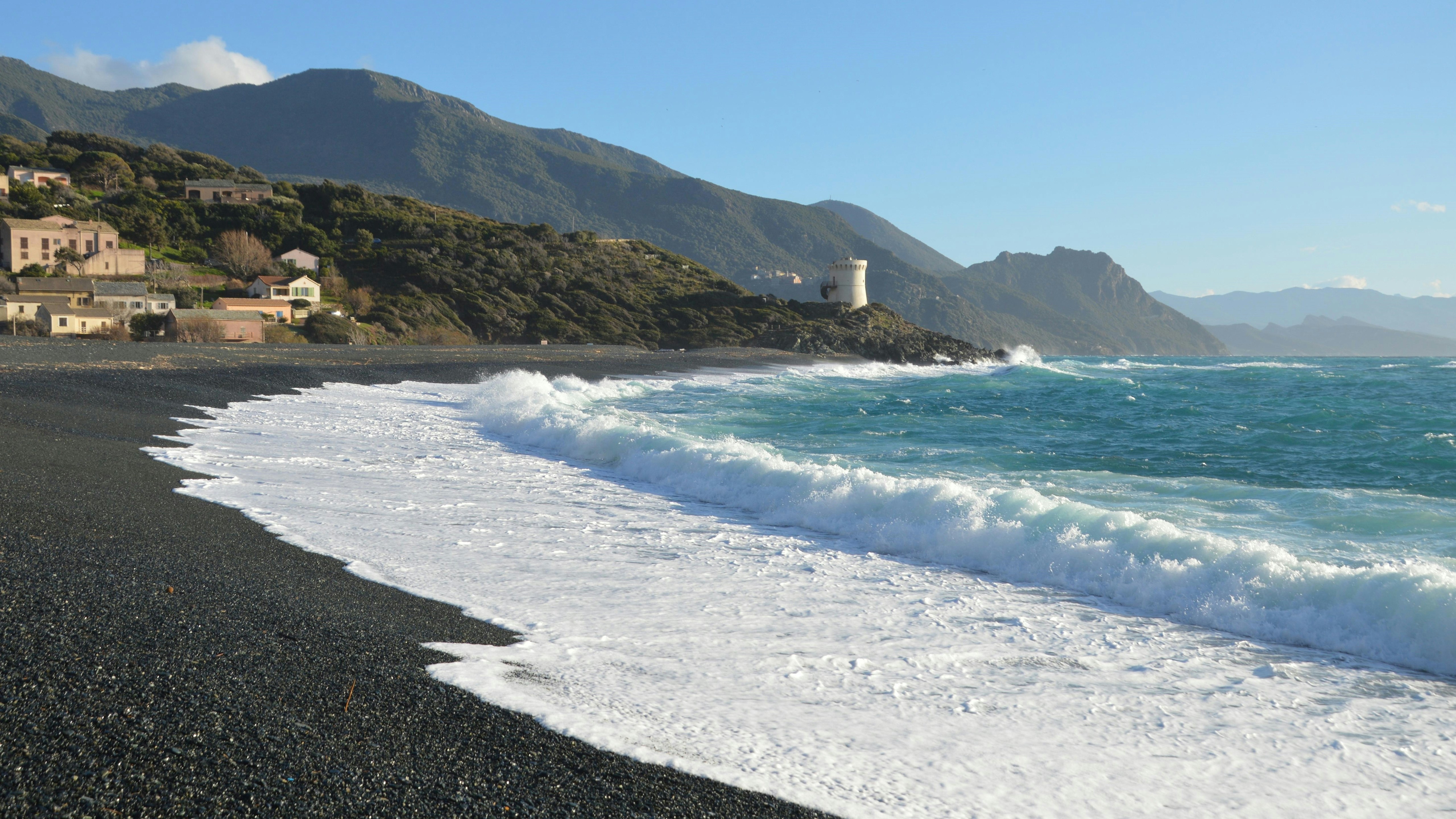 Waves crash on a pebble beach with a lighthouse.