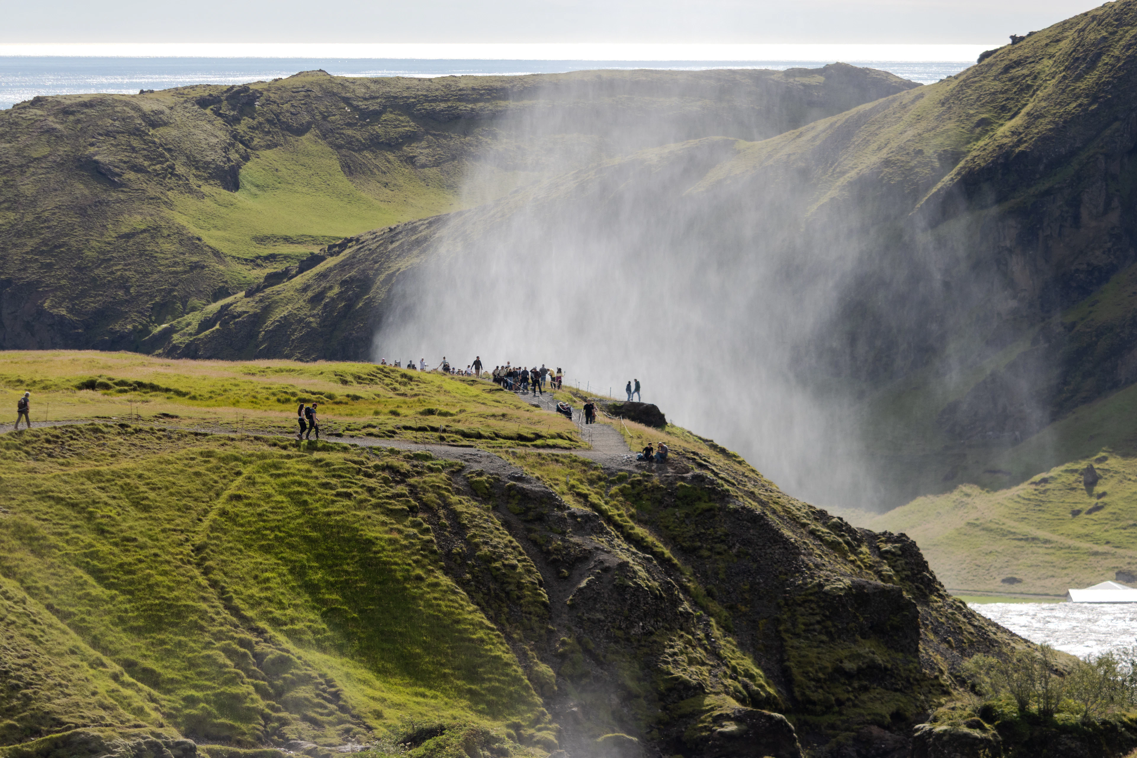 People on a green clifftop watching a powerful waterfall on the south coast