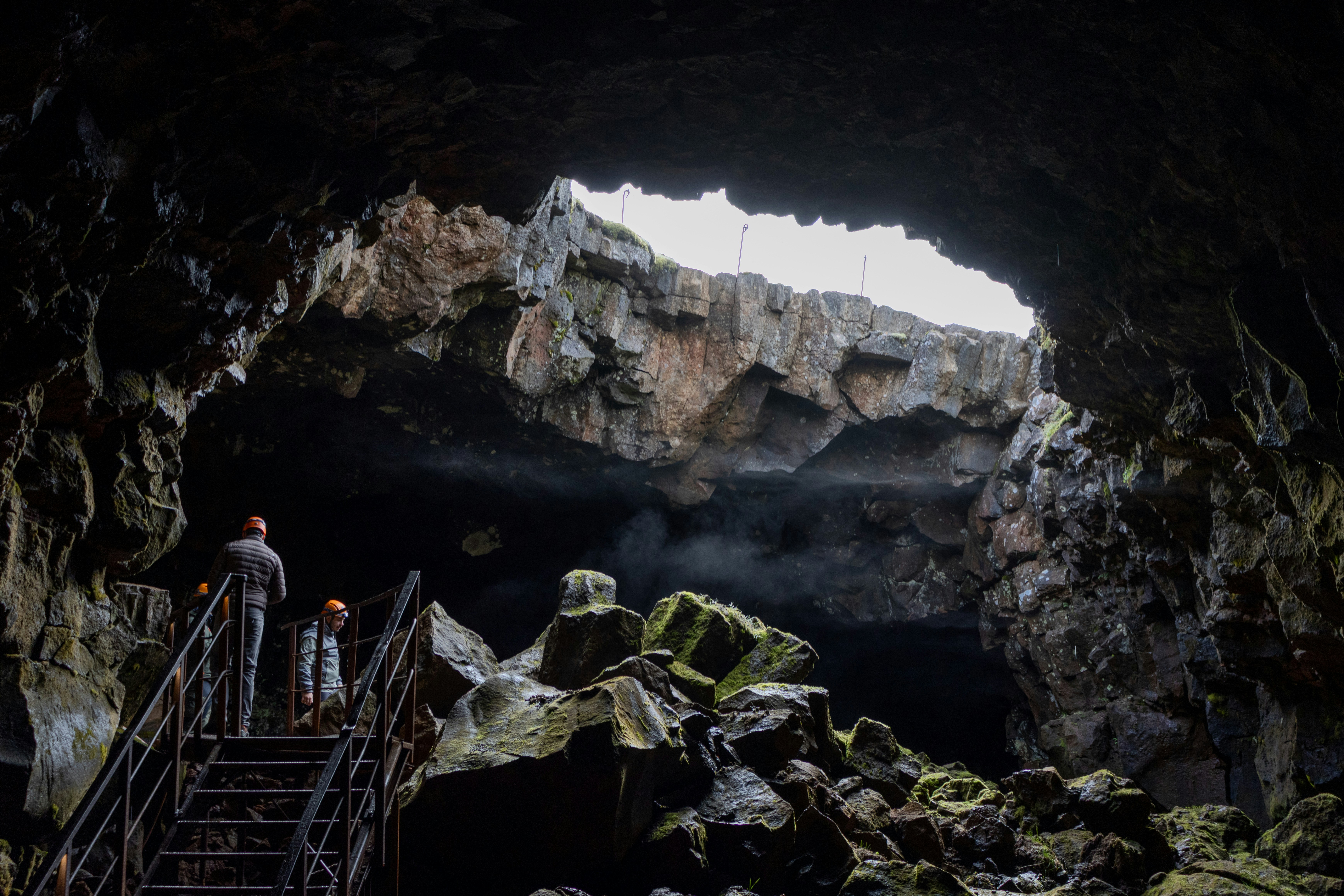 People walk down stairs into a dark cave opening.