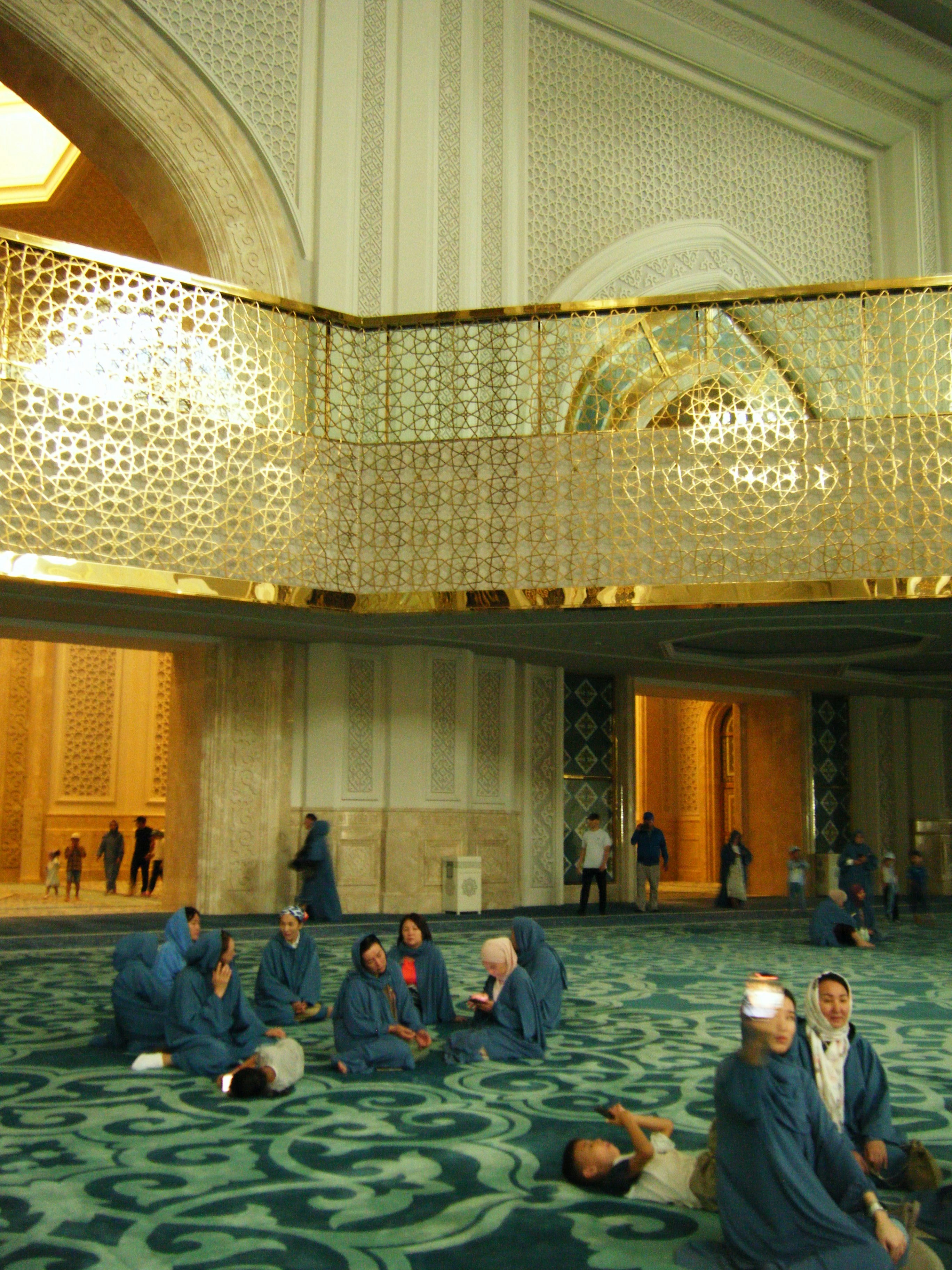 People relaxing on a patterned carpet inside a mosque.
