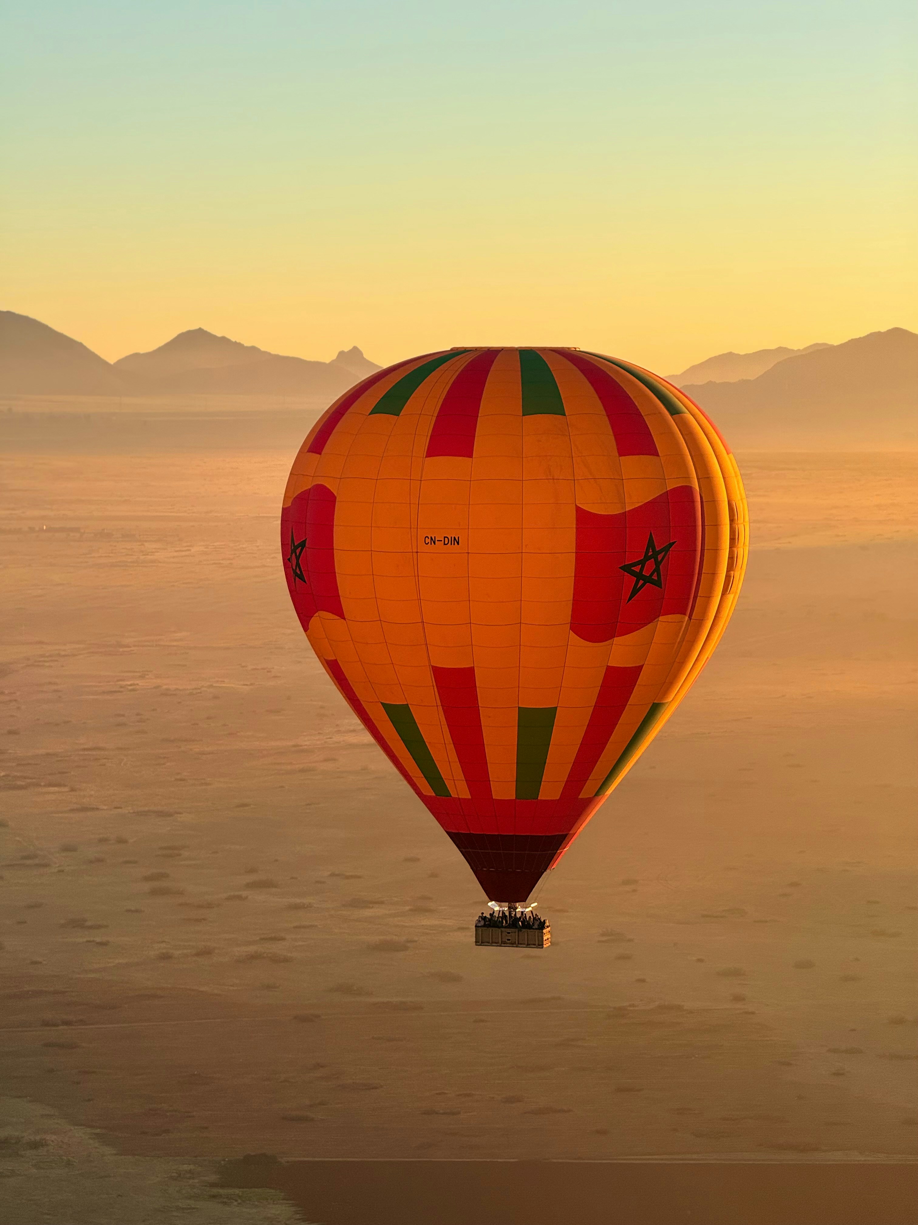 Hot air balloon floats over desert landscape at sunrise.