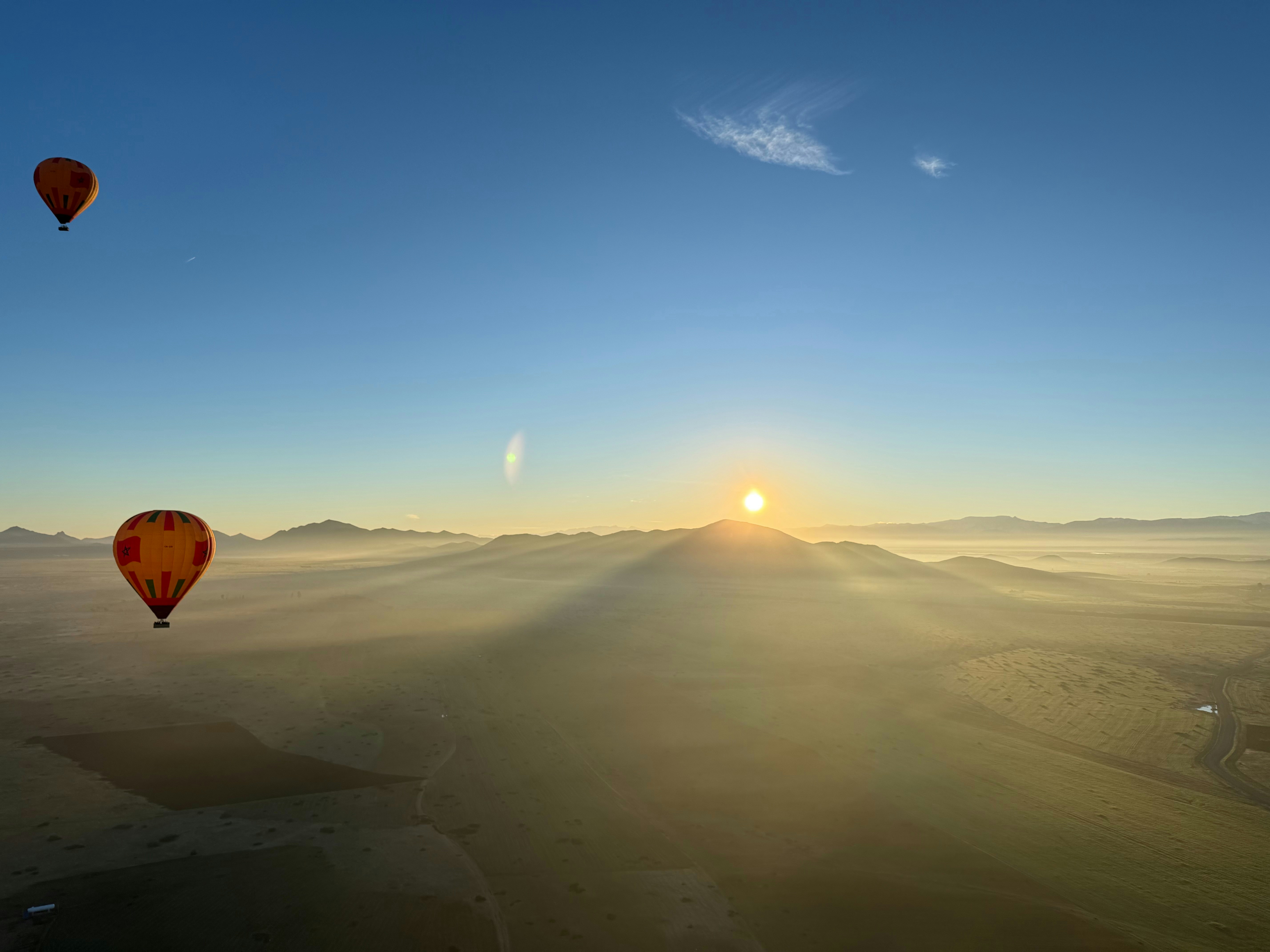 Hot air balloons float over misty mountains at sunrise.