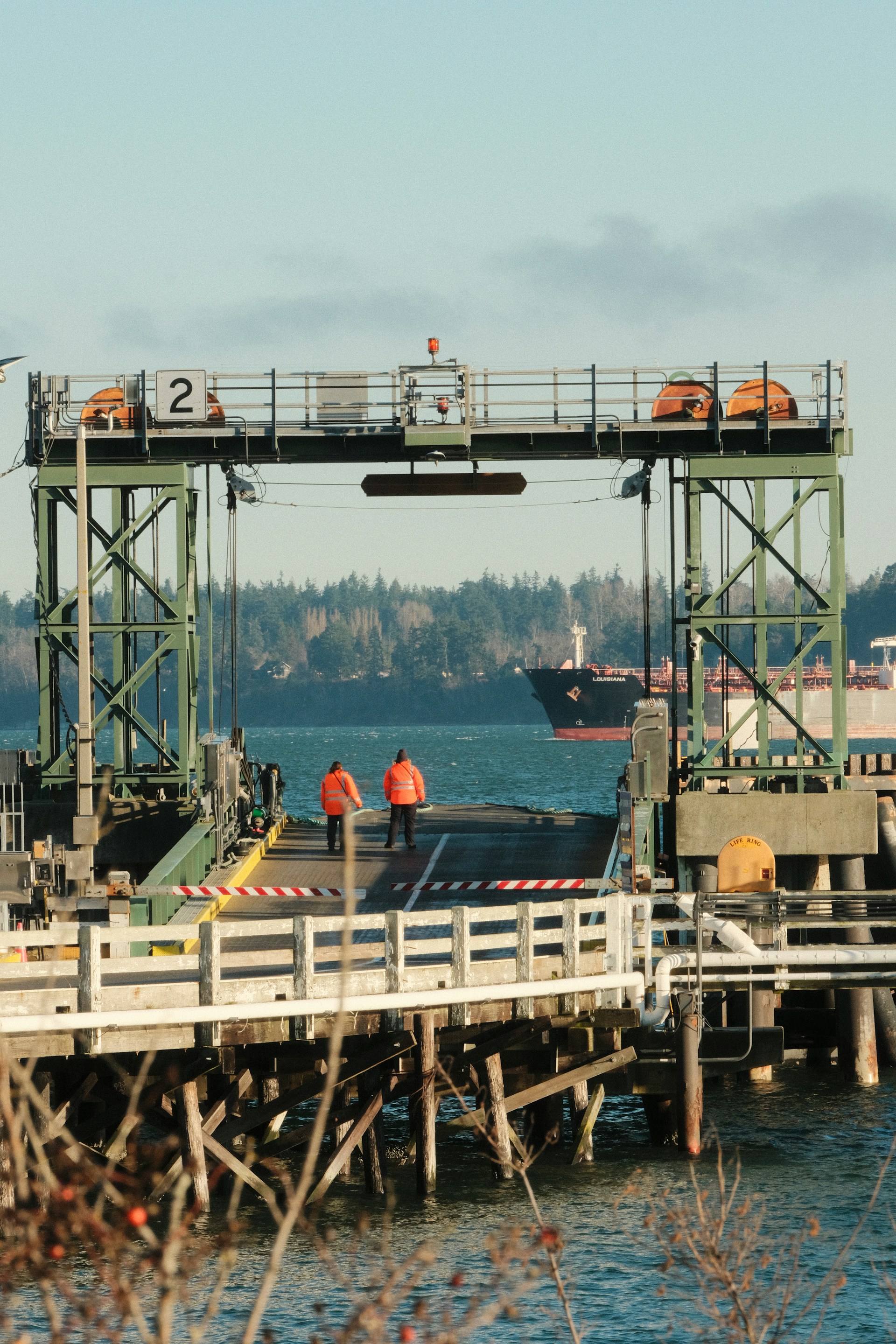 Two people in orange vests walk on a ferry ramp.