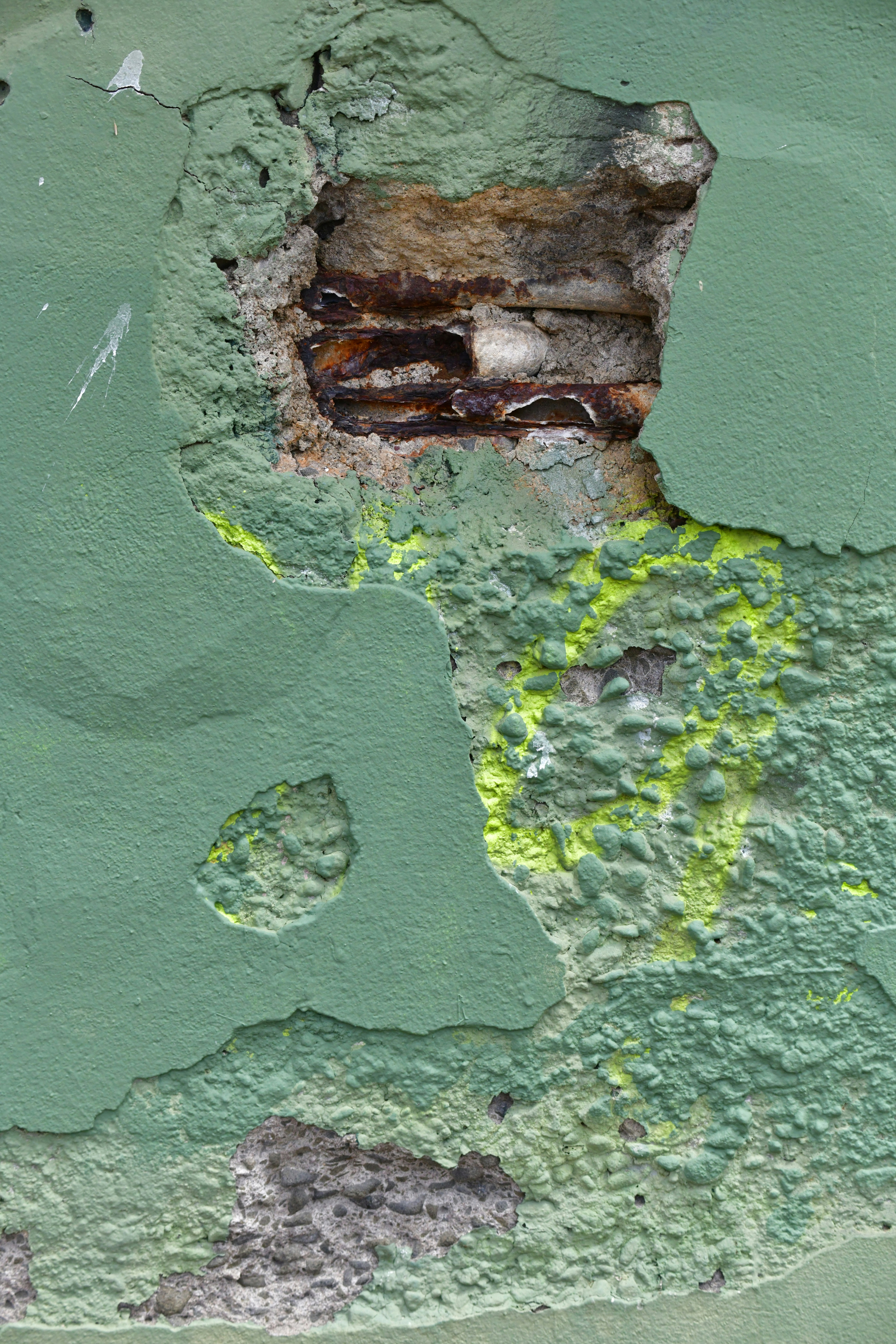 Damaged green wall with exposed rebar and rust.