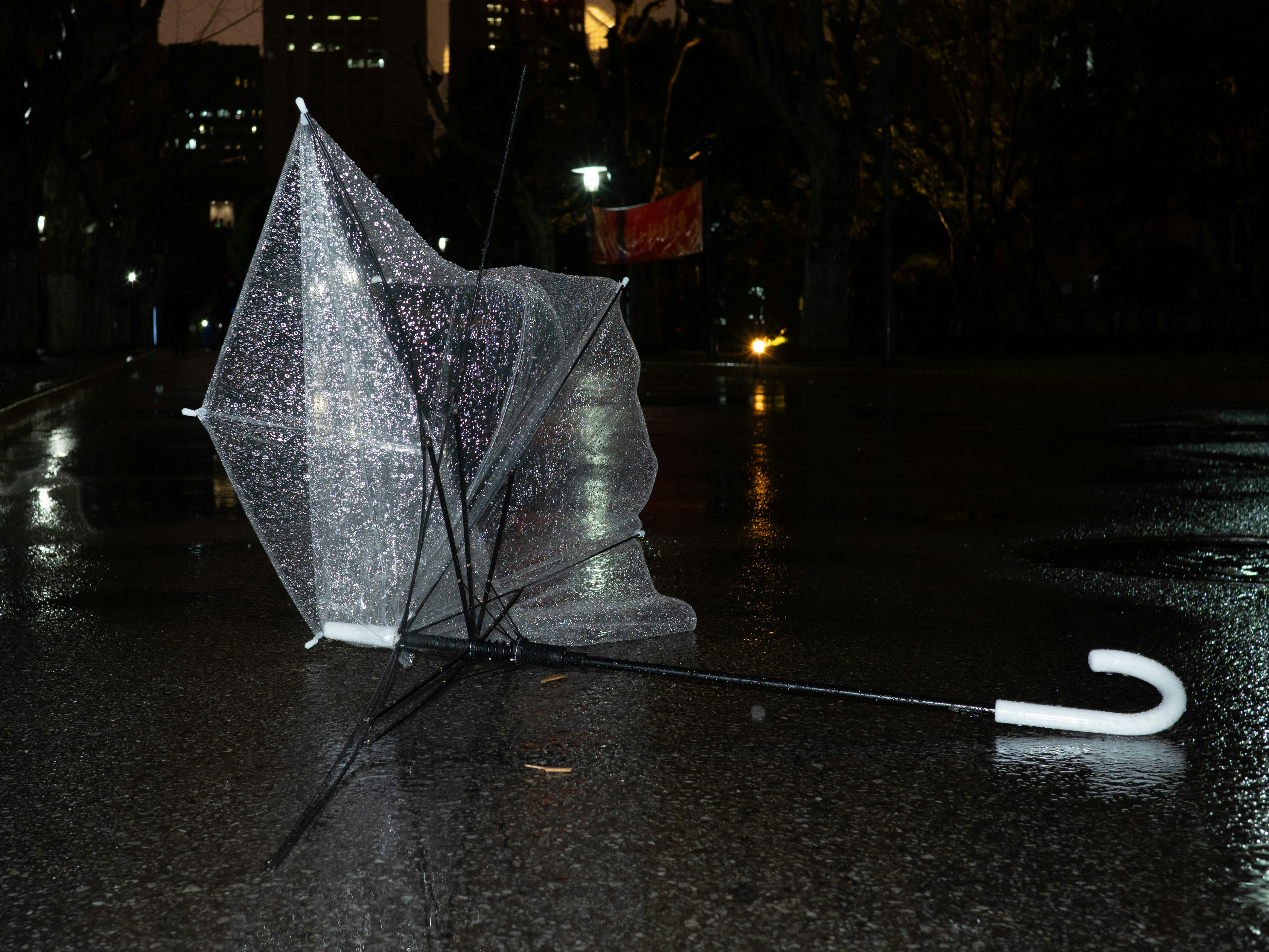Un paraguas roto yace en una calle mojada por la noche.