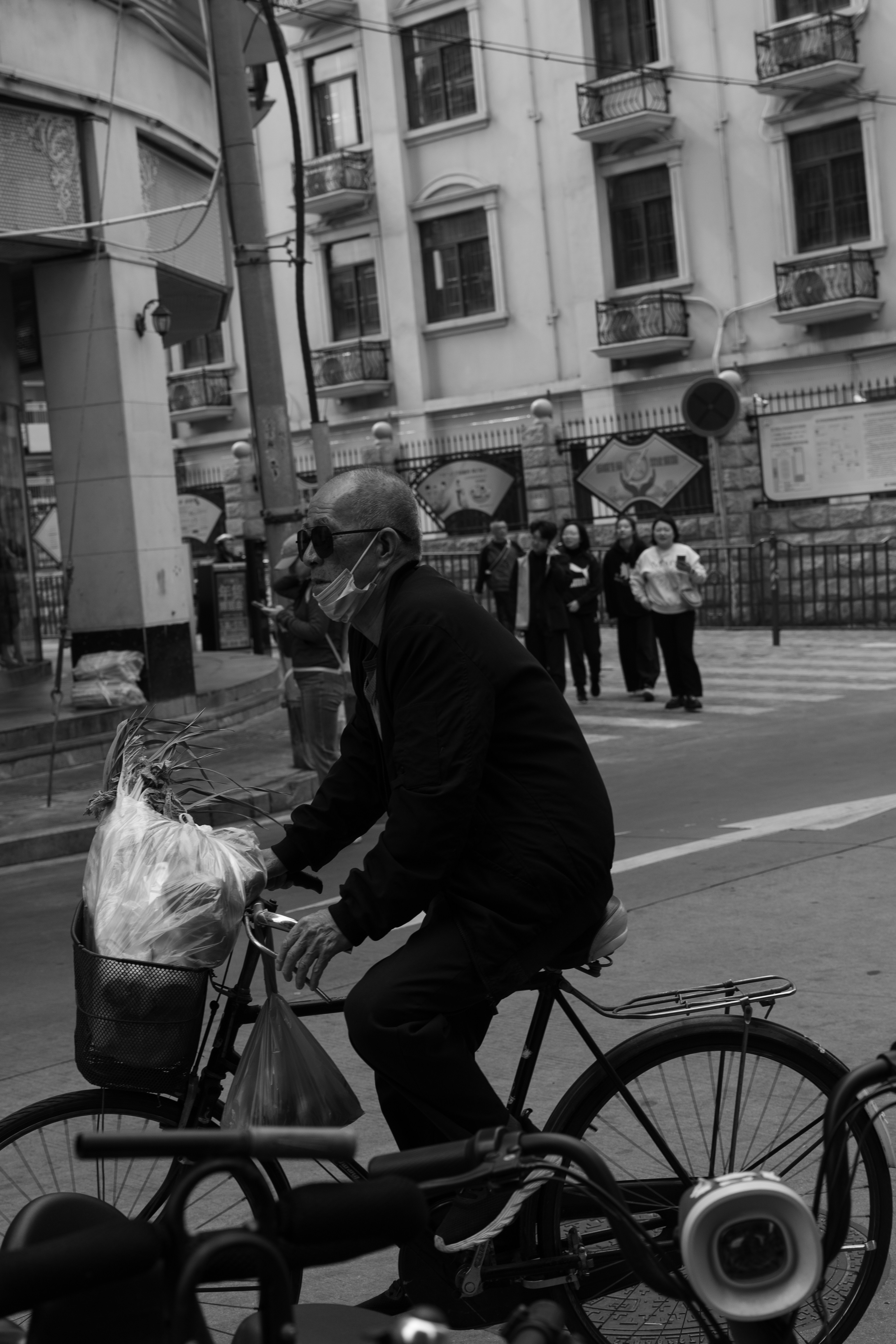Elderly man rides bicycle with mask and groceries.