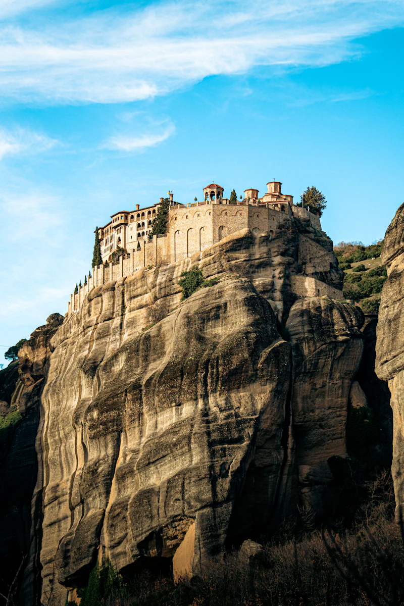 A monastery perched on a rock cliff under blue sky