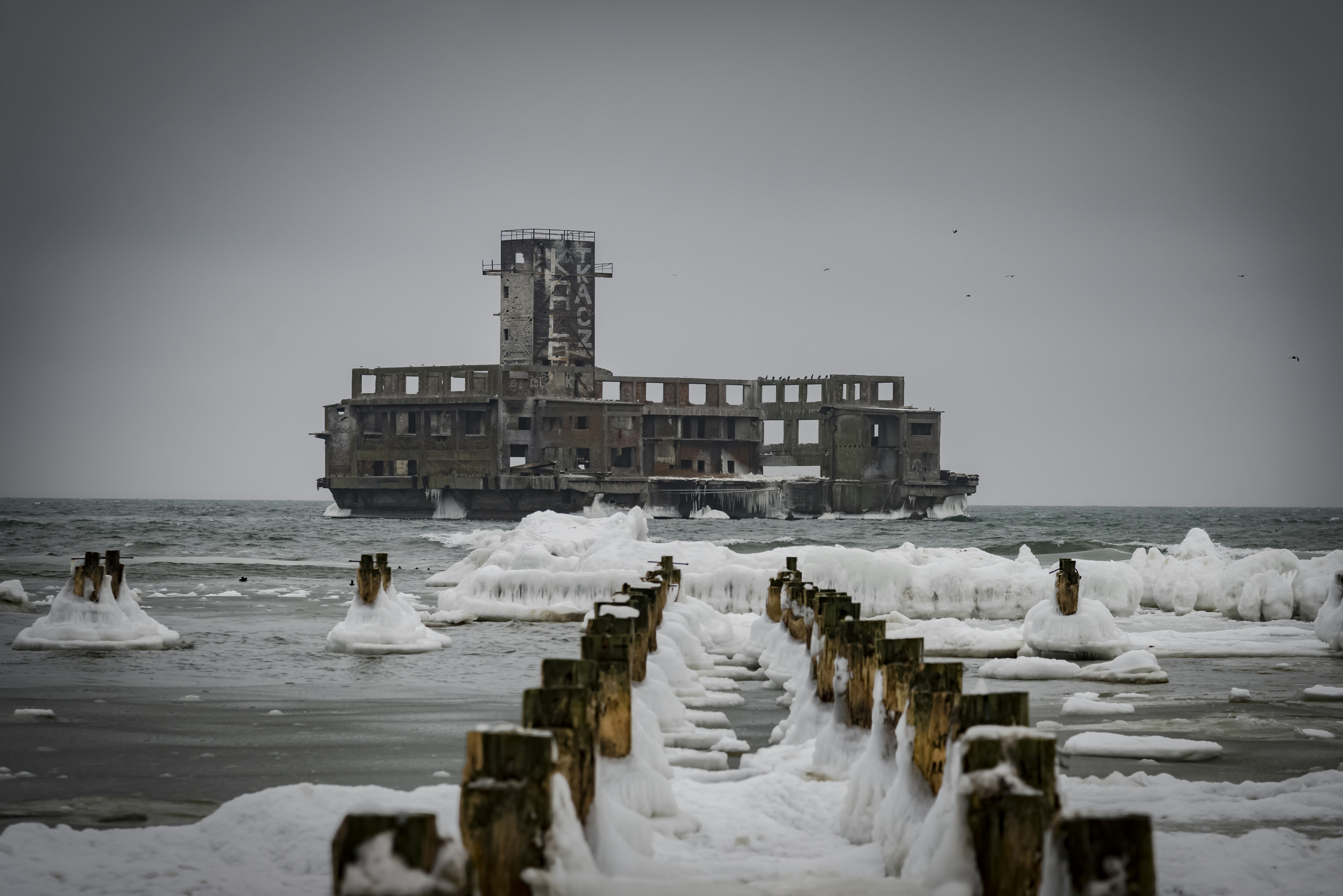 Derelict building in icy water with wooden posts