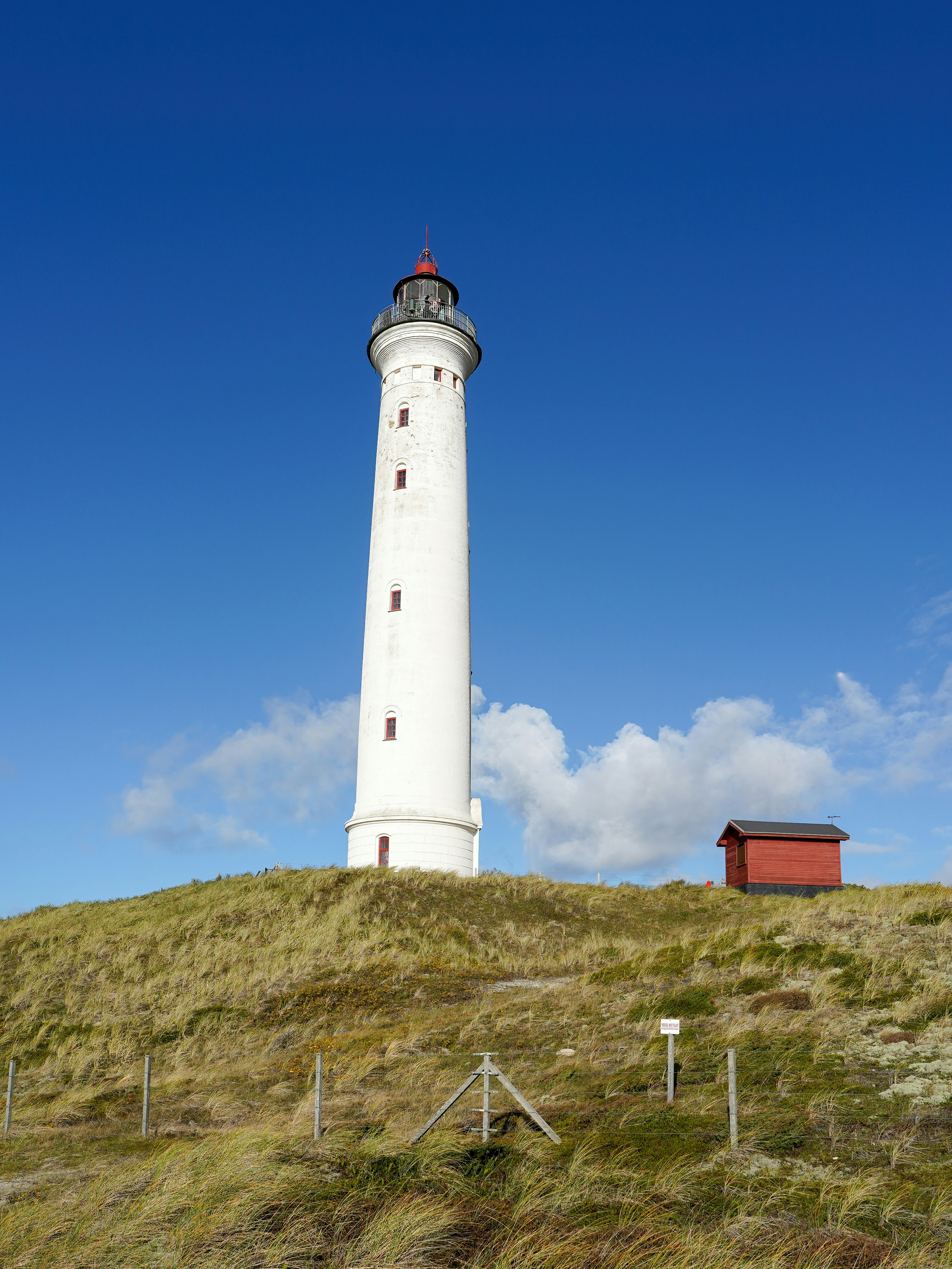 White lighthouse on a grassy hill under blue sky.