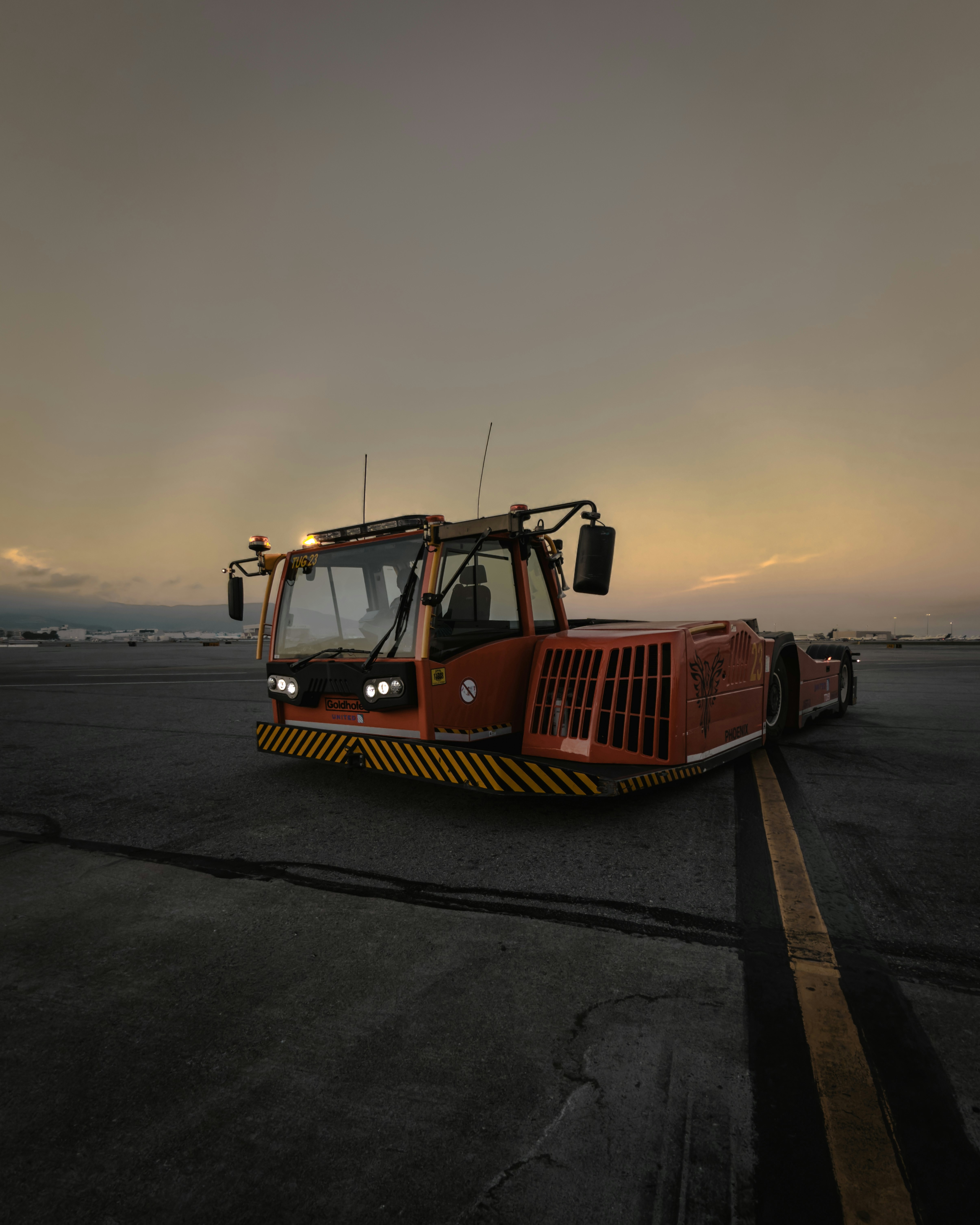 Trator de reboque laranja no asfalto do aeroporto ao entardecer
