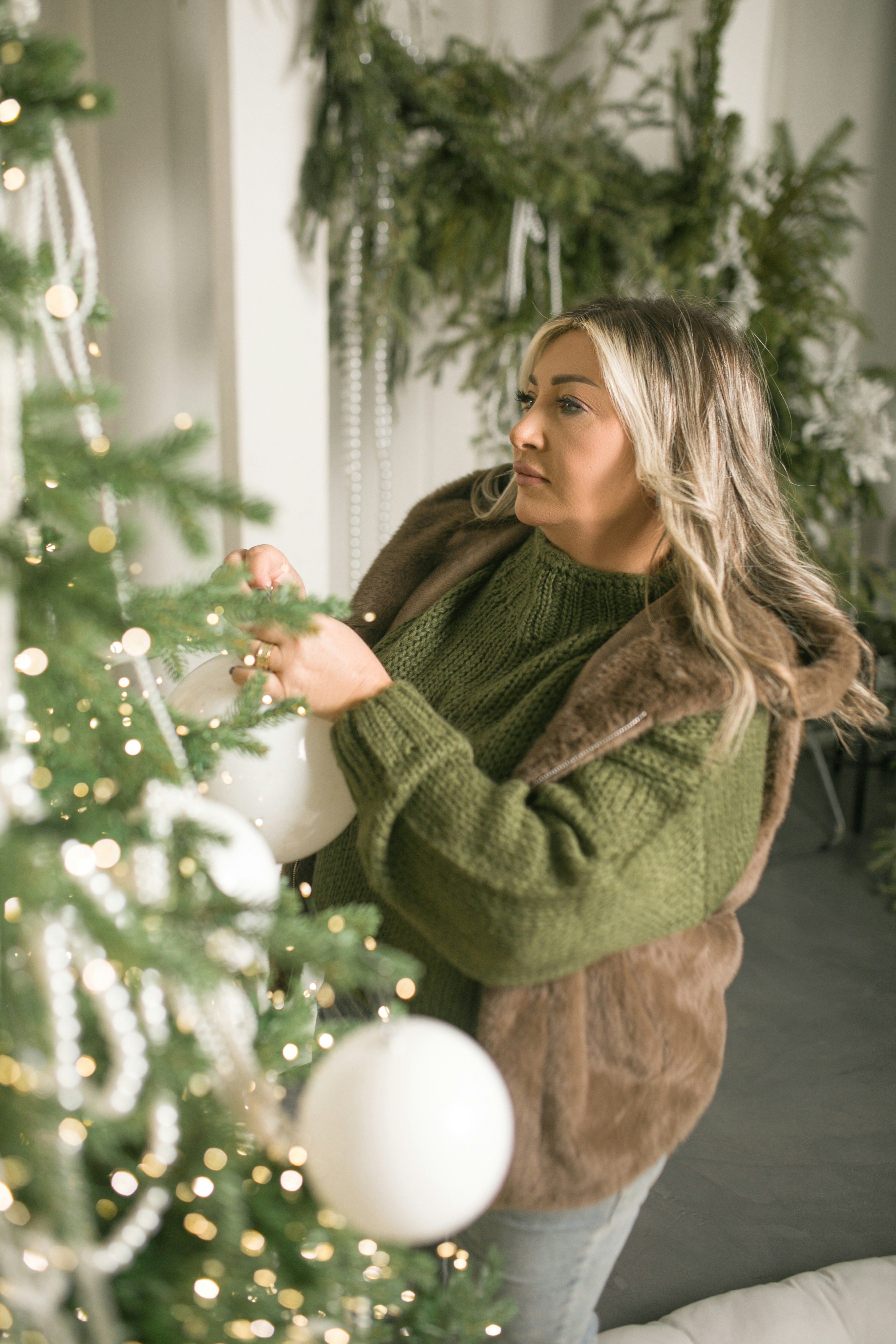 A woman decorates a christmas tree with ornaments.