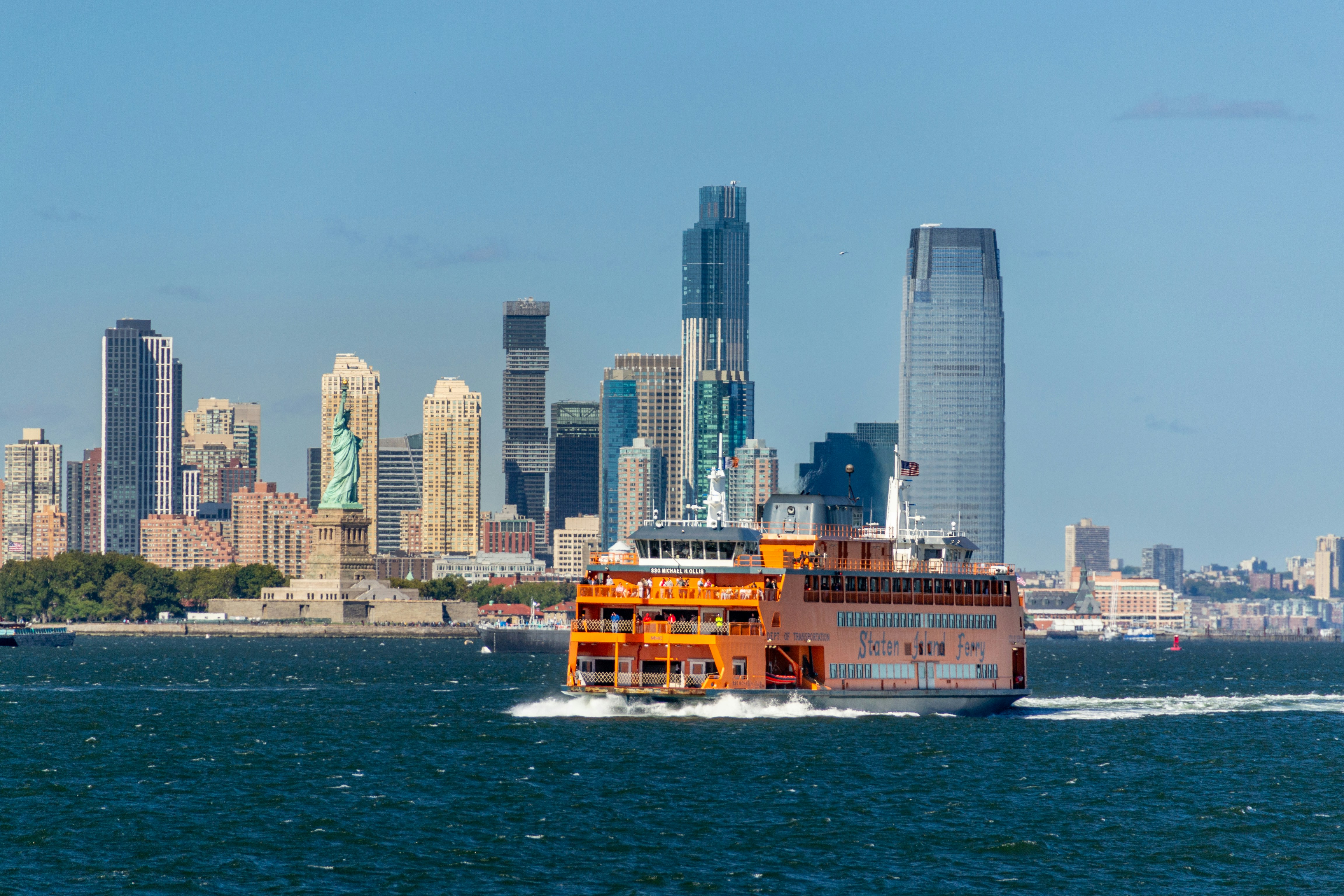 Un traghetto arancione passa davanti alla Statua della Libertà e allo skyline.