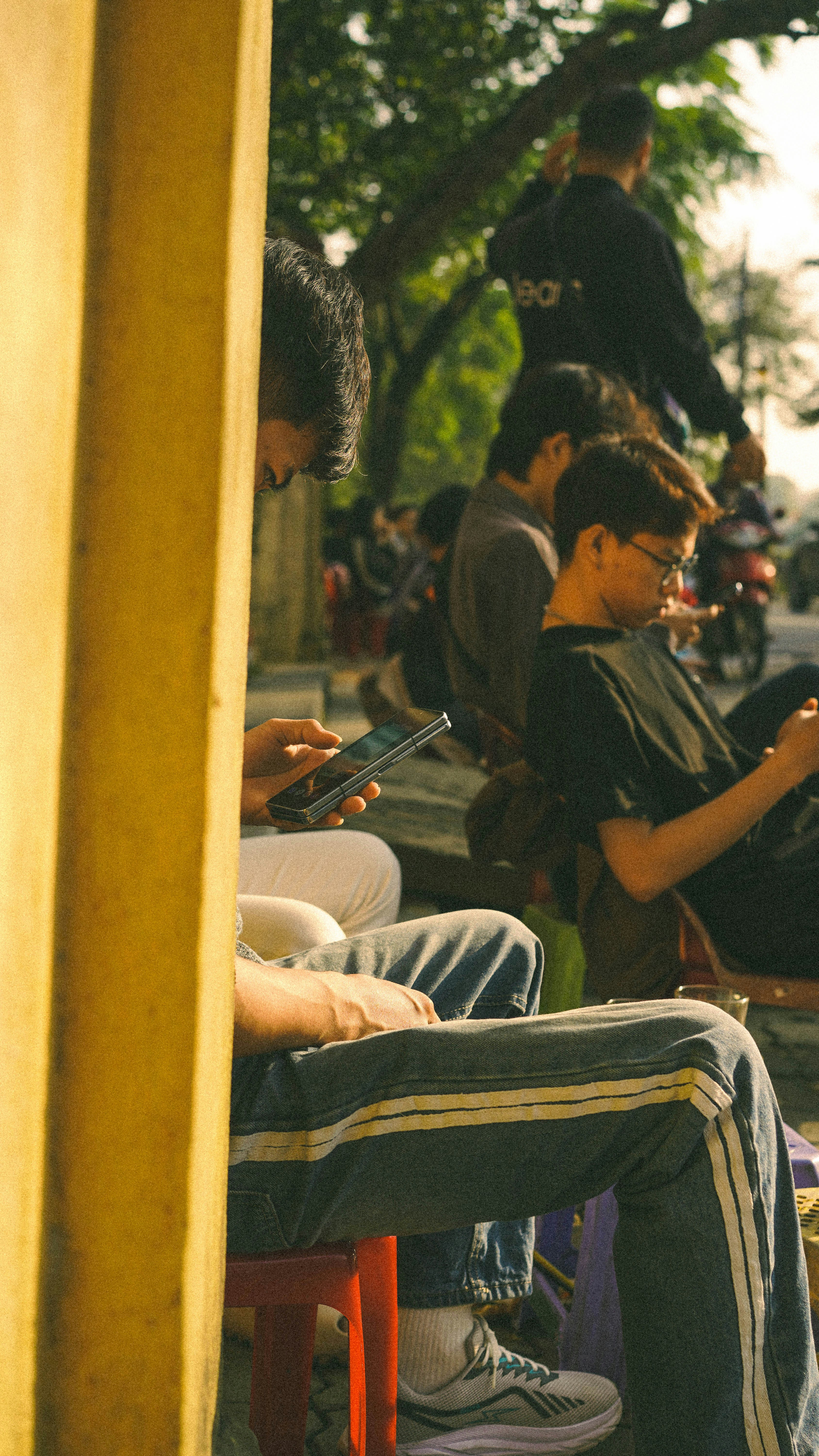 Orang-orang duduk dan melihat ponsel mereka di luar ruangan