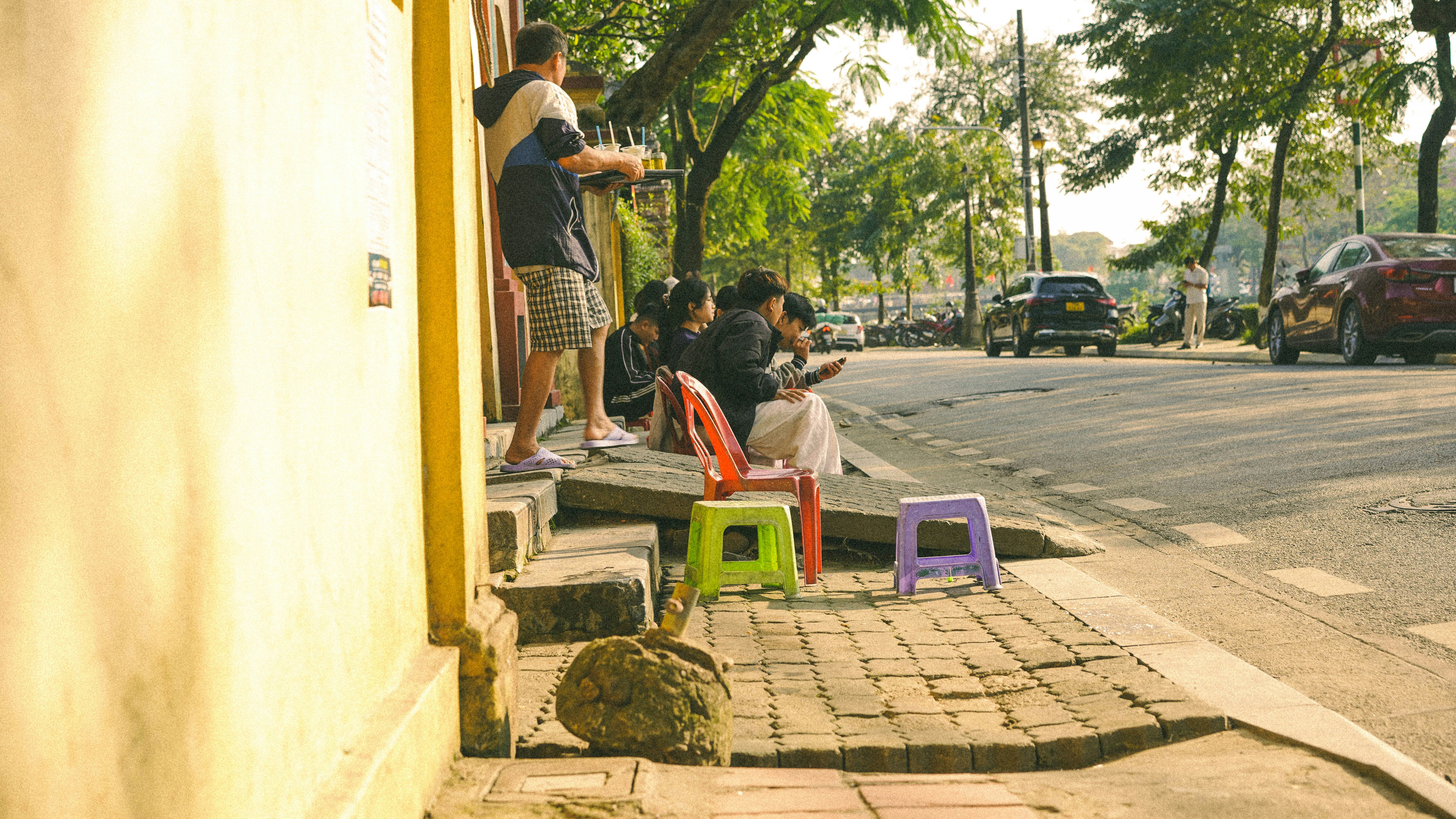 People sitting on colorful stools by a sunny street.