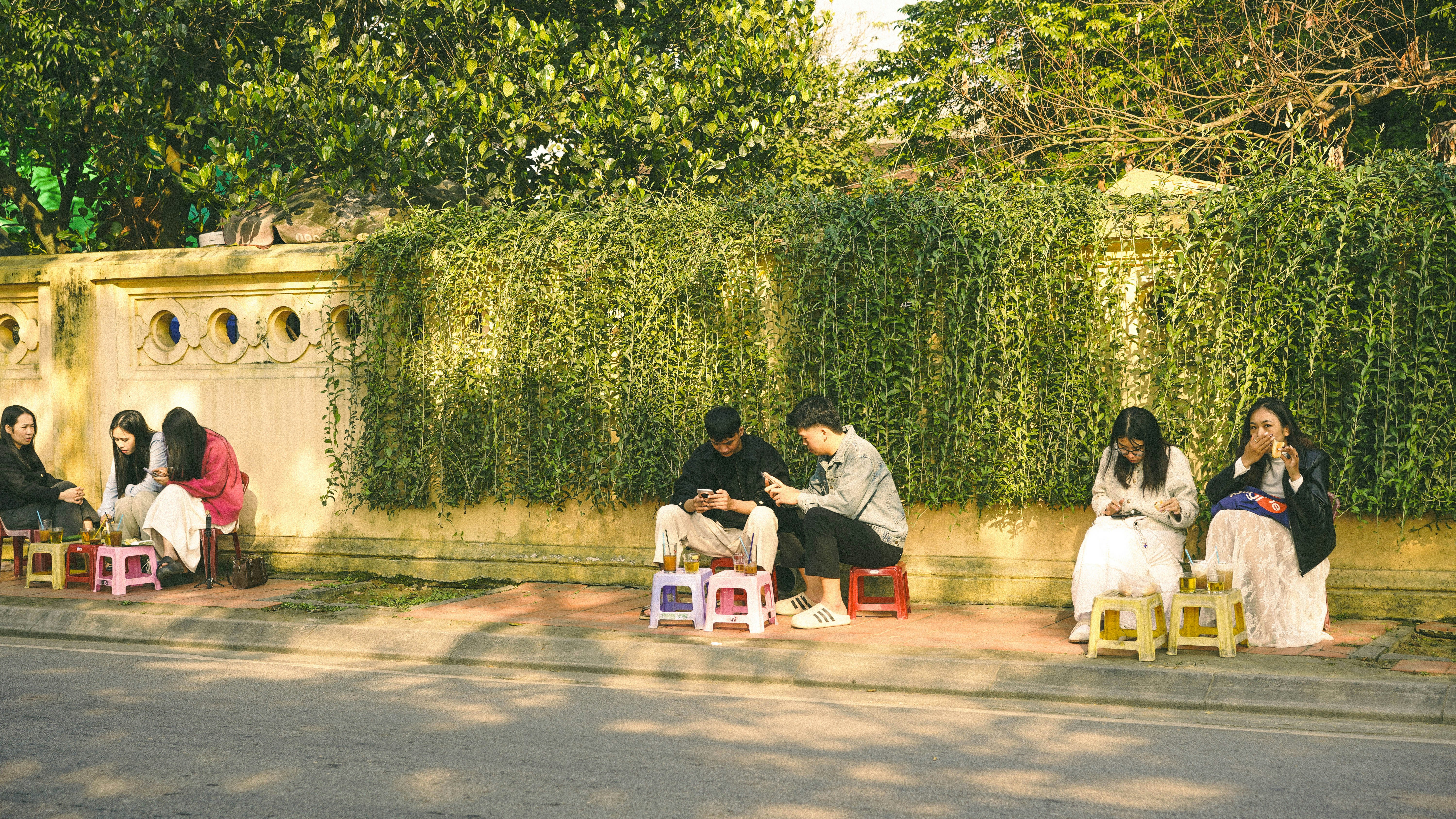People sitting on small stools by a wall.