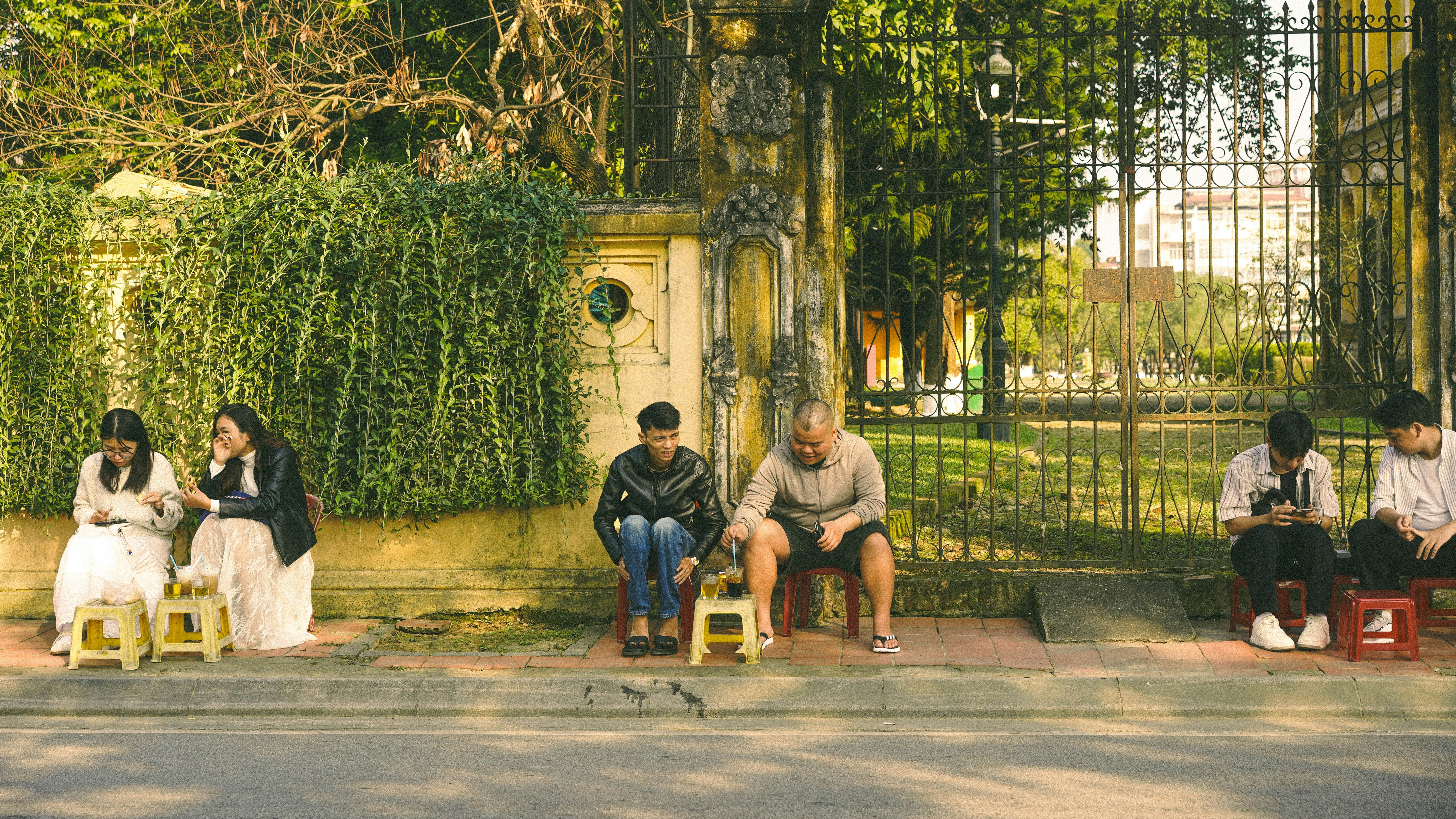 People sitting on small stools by a fence
