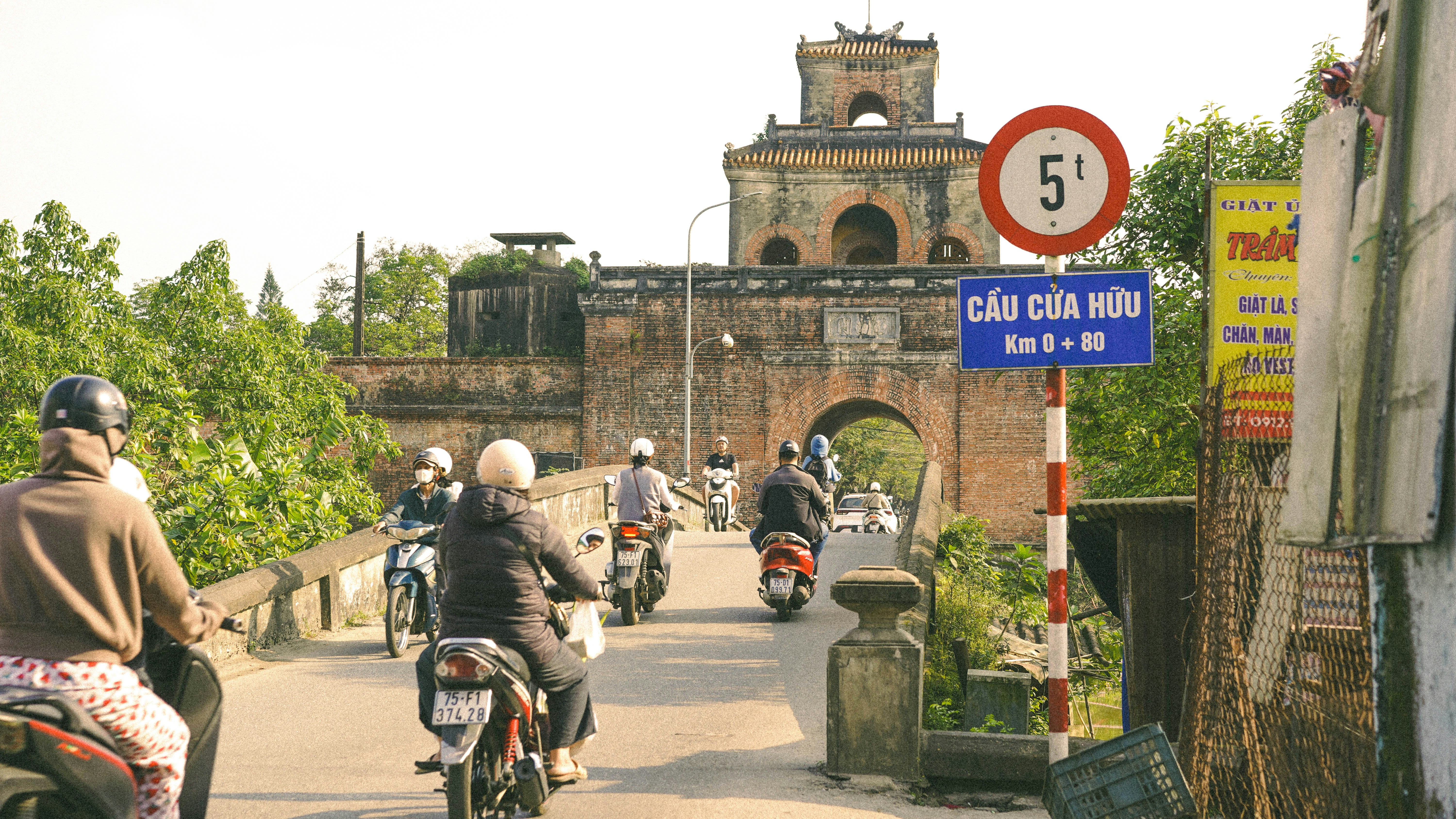 Motorcycles crossing a bridge towards an ancient gate.