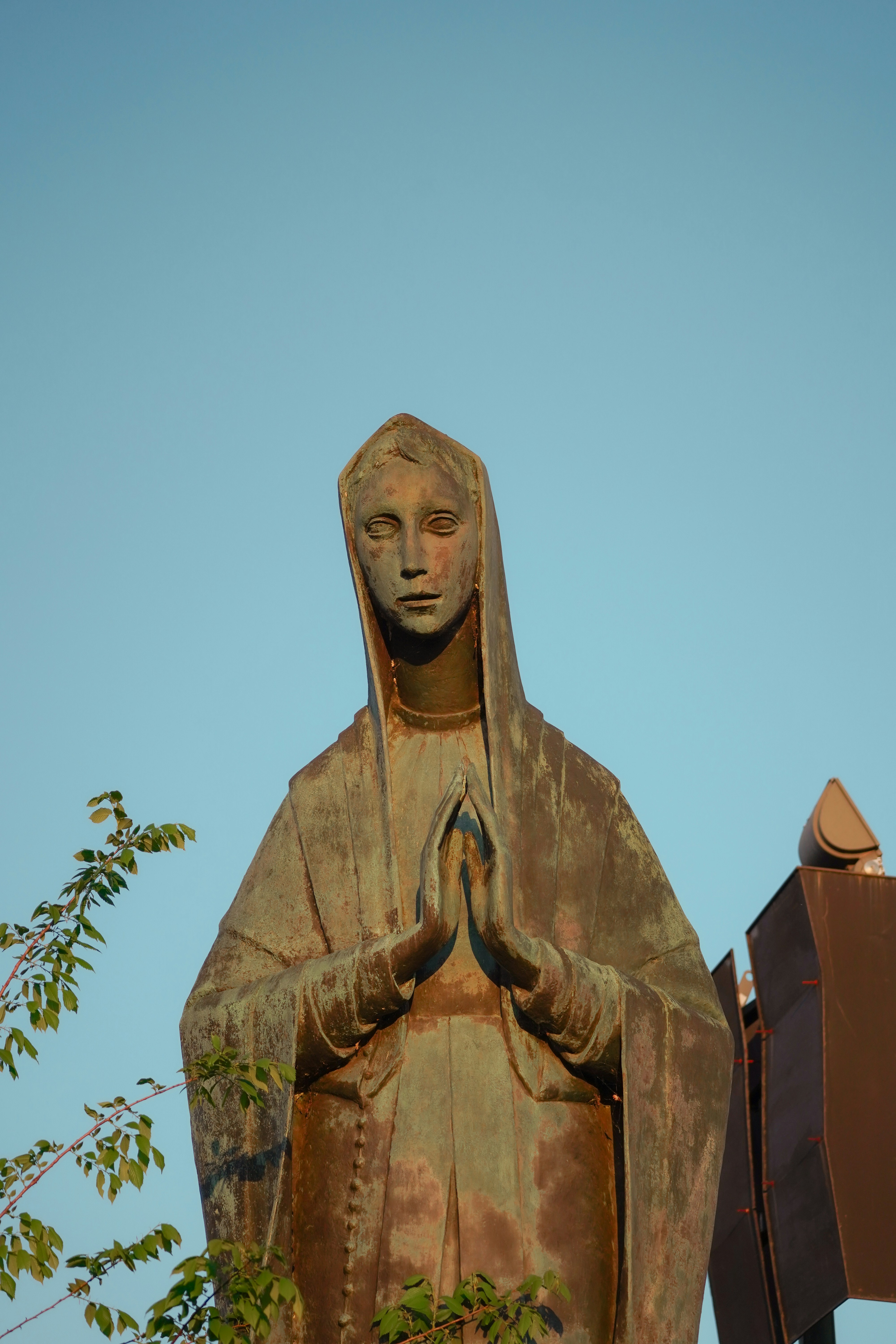 A weathered bronze statue of a praying woman.