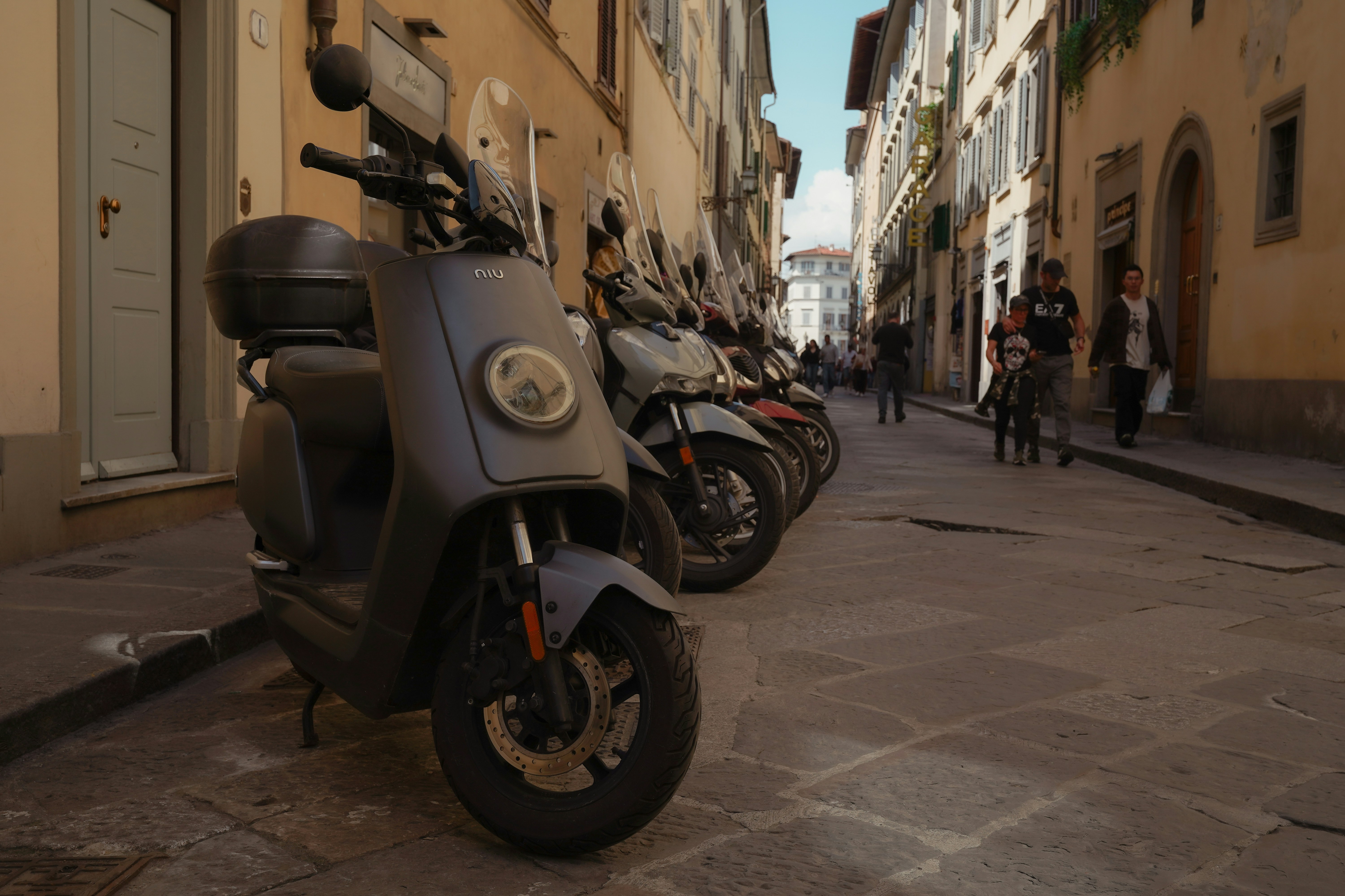 Several parked scooters on a cobblestone street.