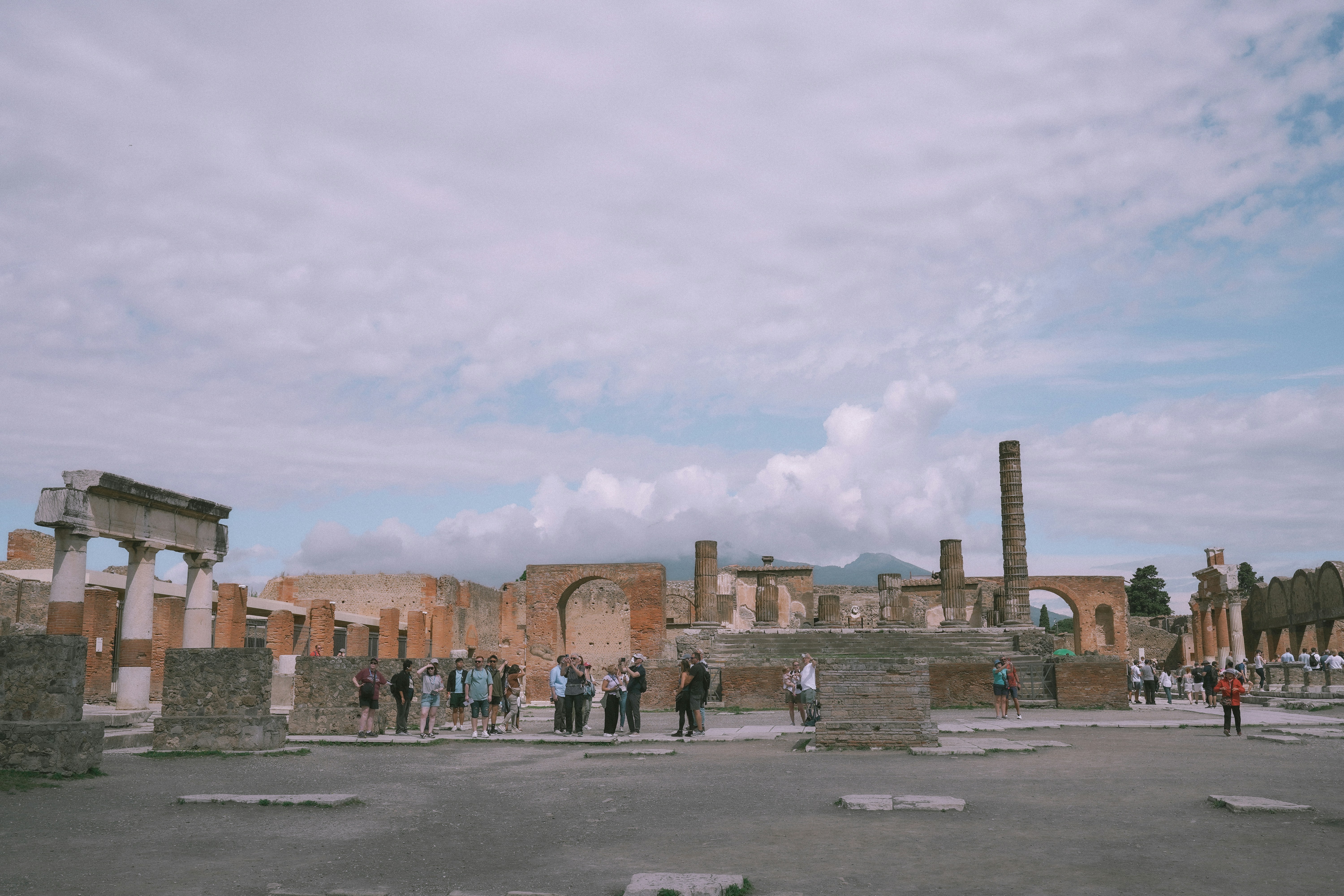 Ancient roman ruins with scattered tourists under cloudy sky