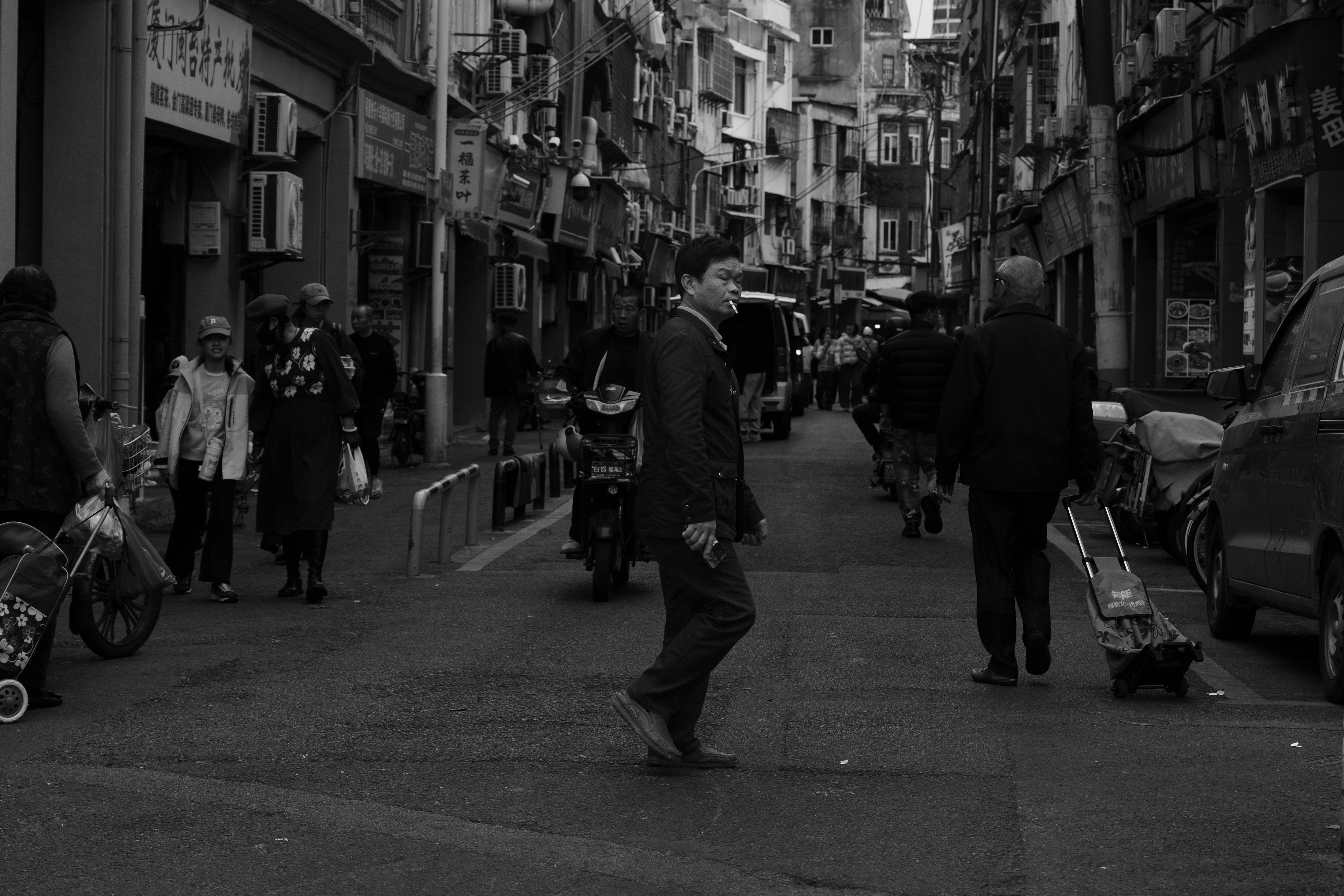 People walk down a narrow, bustling city street.