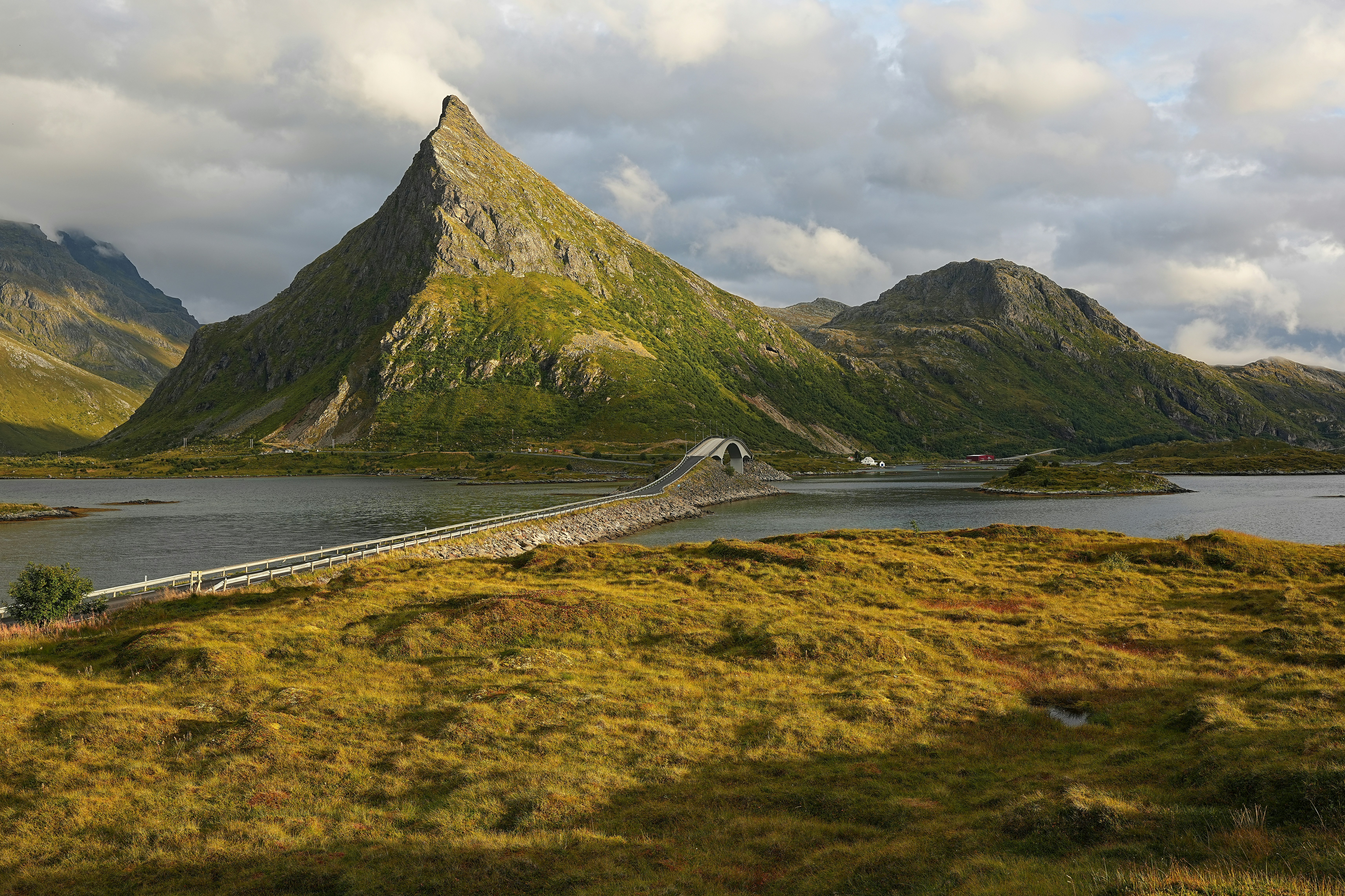 A scenic bridge crosses a calm lake towards mountains