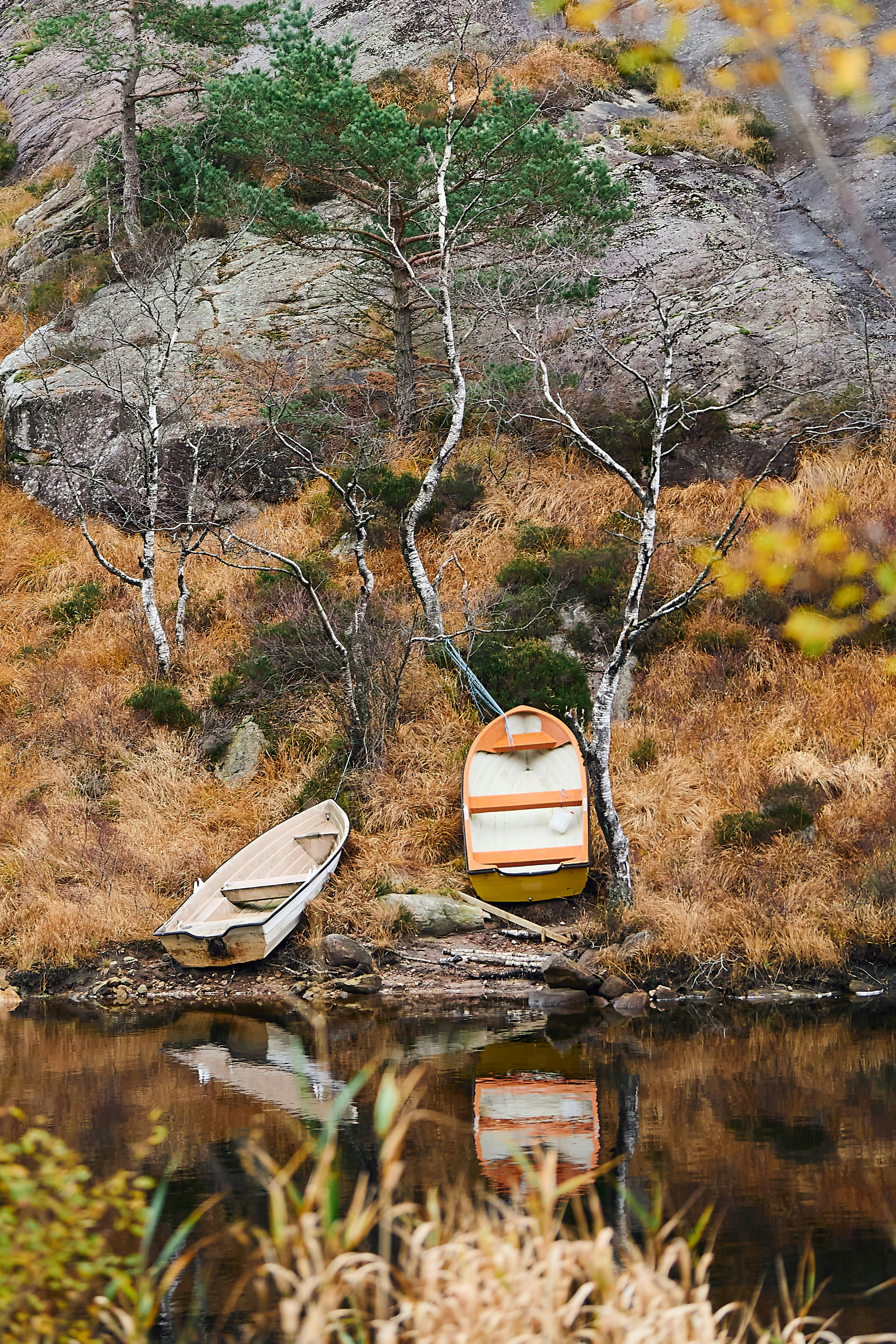 Two boats rest by a calm lake with autumn foliage.