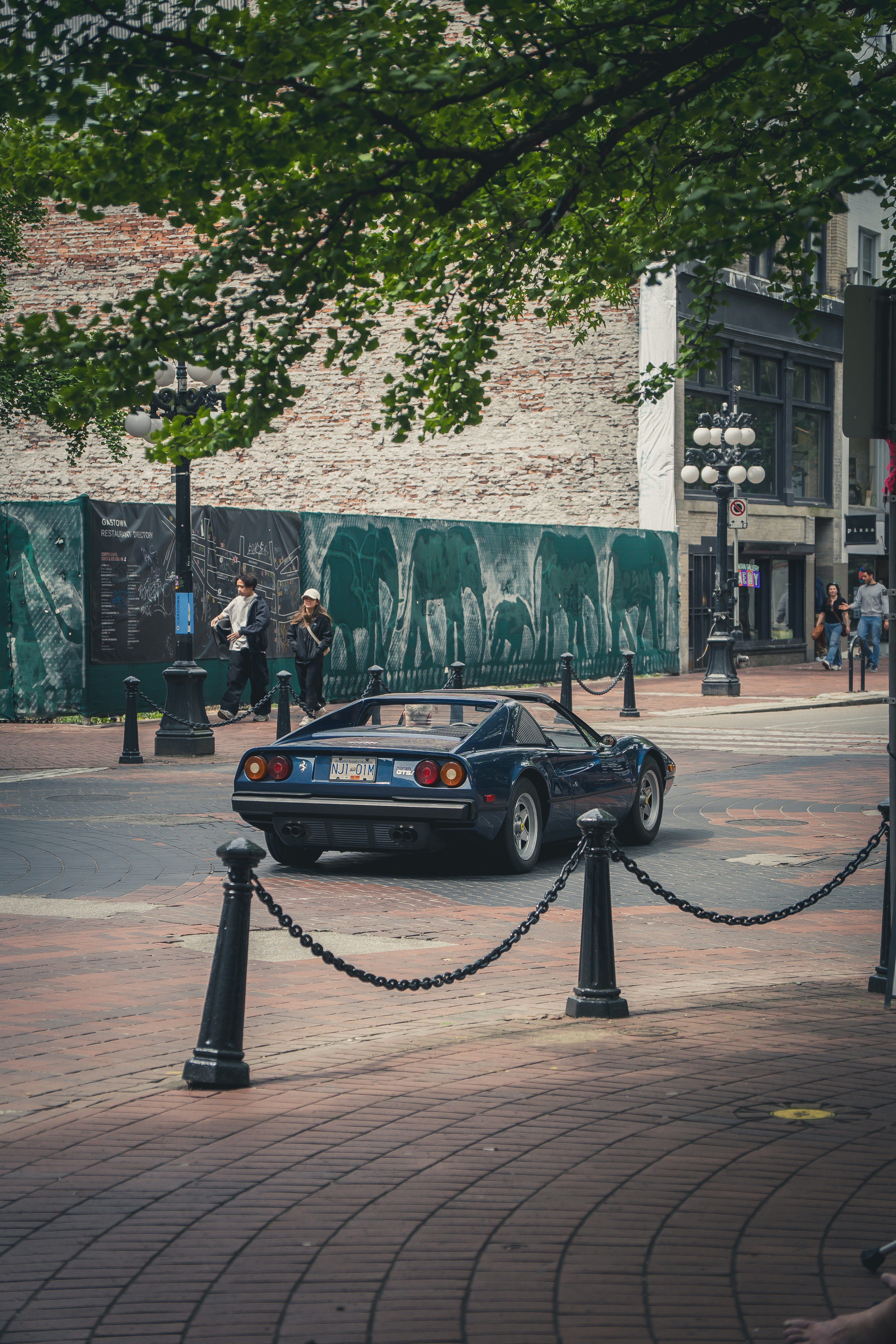 A dark blue sports car drives down a brick street