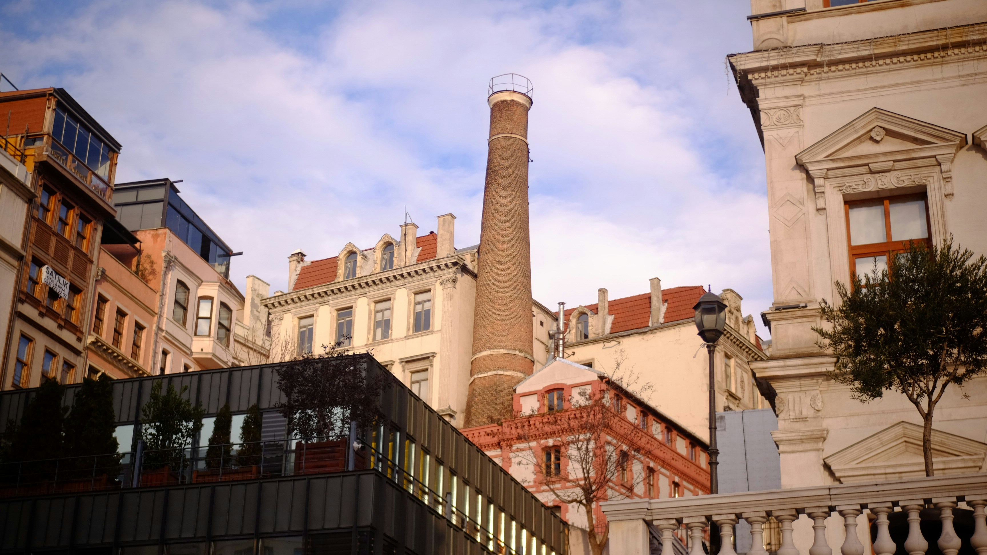 Tall brick chimney among historic buildings and modern glass facade.