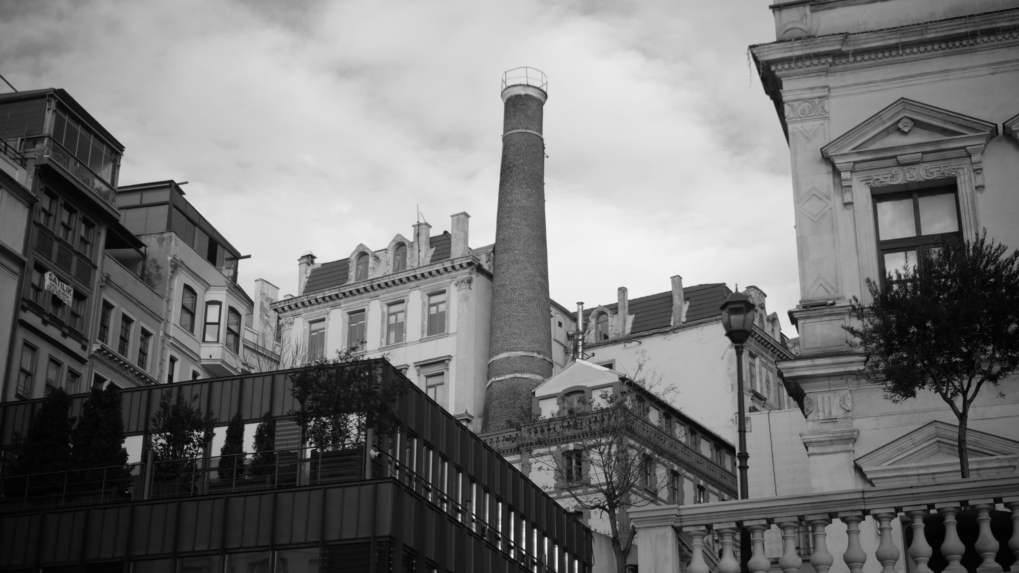Tall brick chimney stands amidst historic buildings under cloudy sky