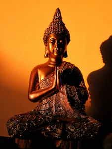 Bronze buddha statue in prayer pose against orange wall