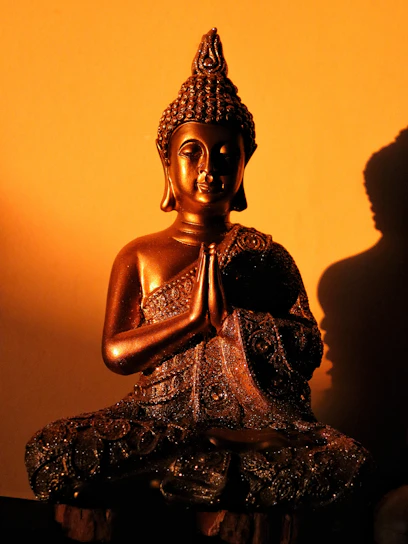 Bronze buddha statue in prayer pose against orange wall