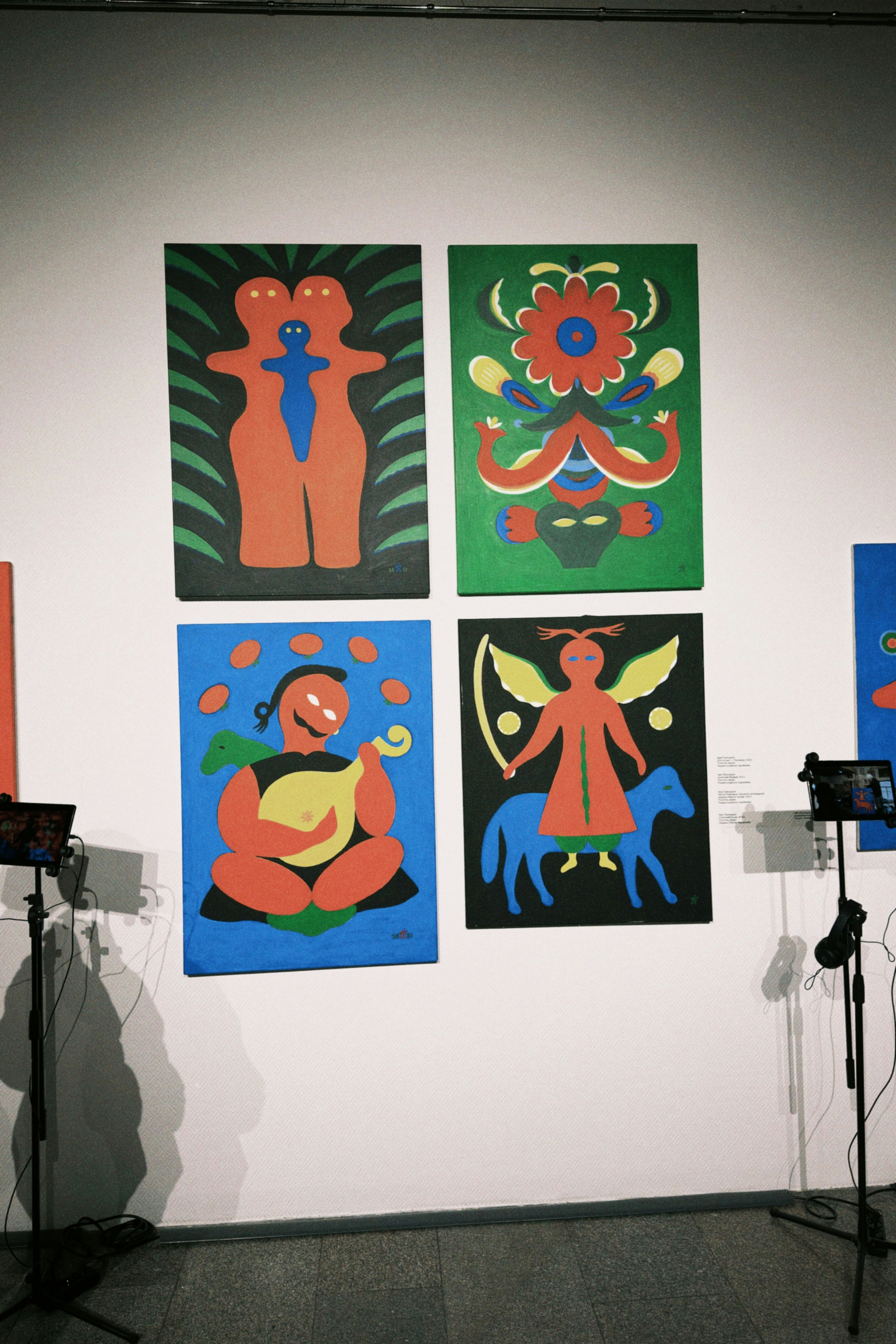 Quatre peintures d’art populaire colorées exposées sur un mur blanc.