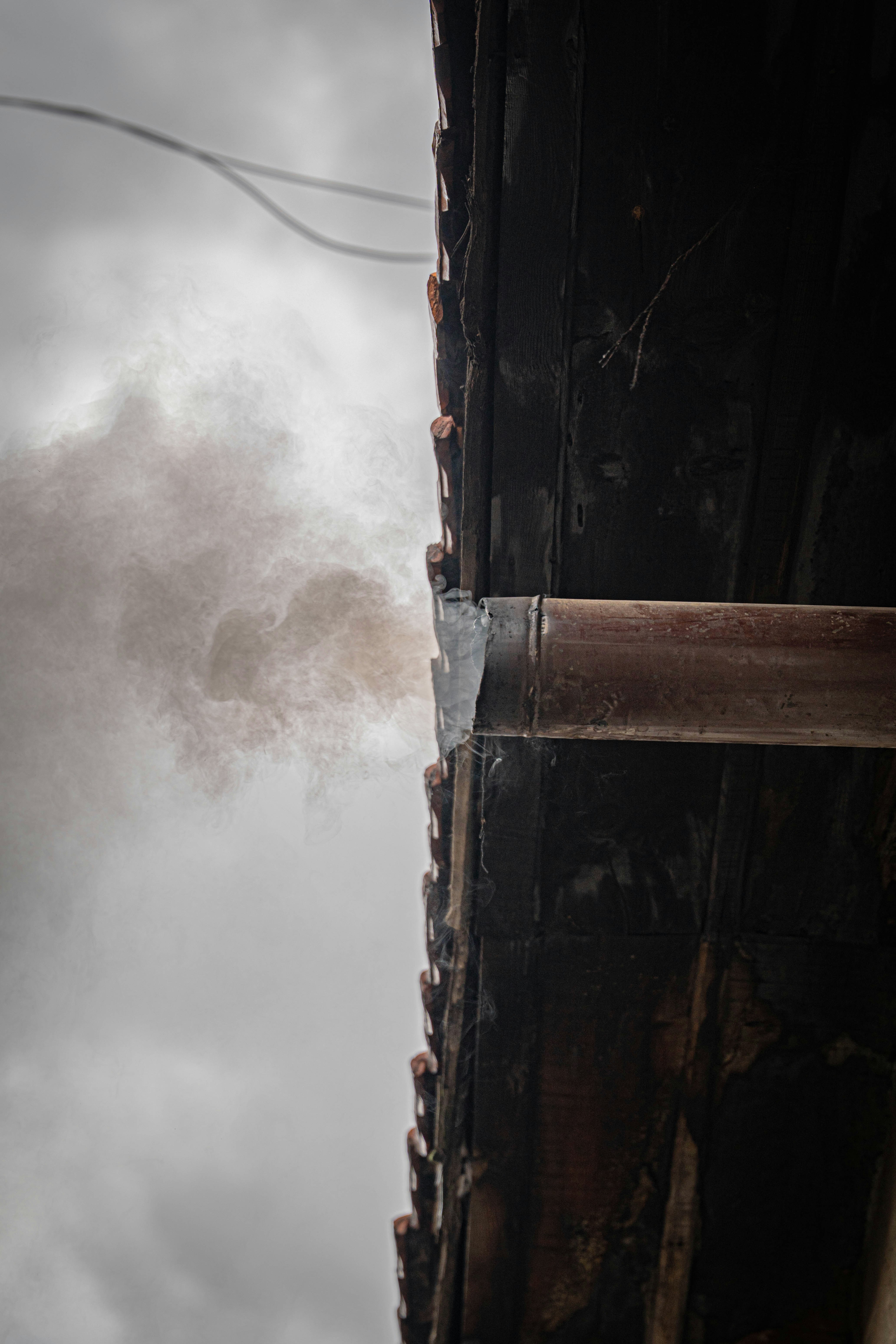 Smoke billowing from a rusty chimney on a cloudy day.