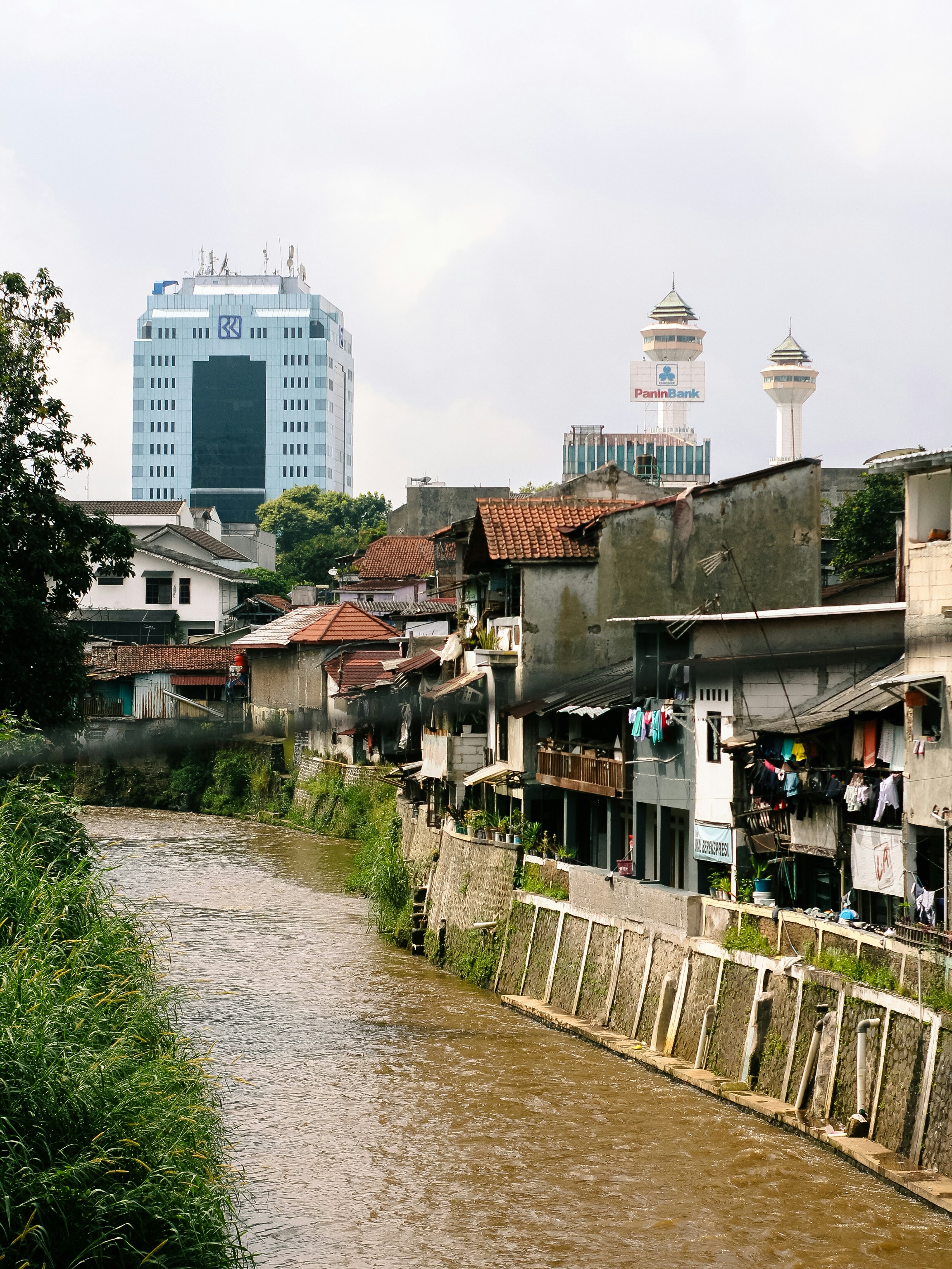 River flows past urban homes and modern buildings.
