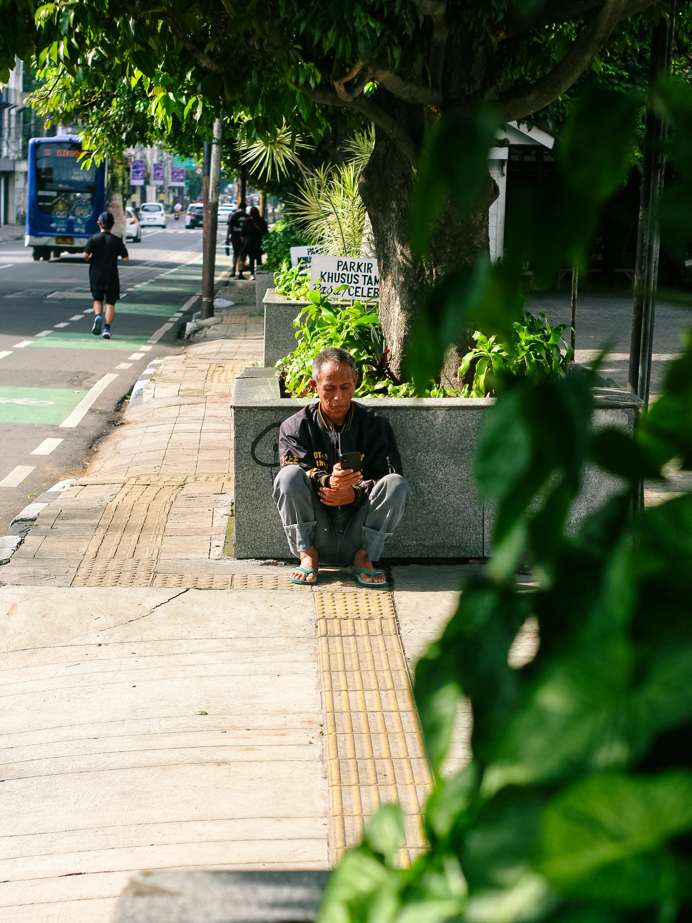 Man sitting on sidewalk next to a tree.