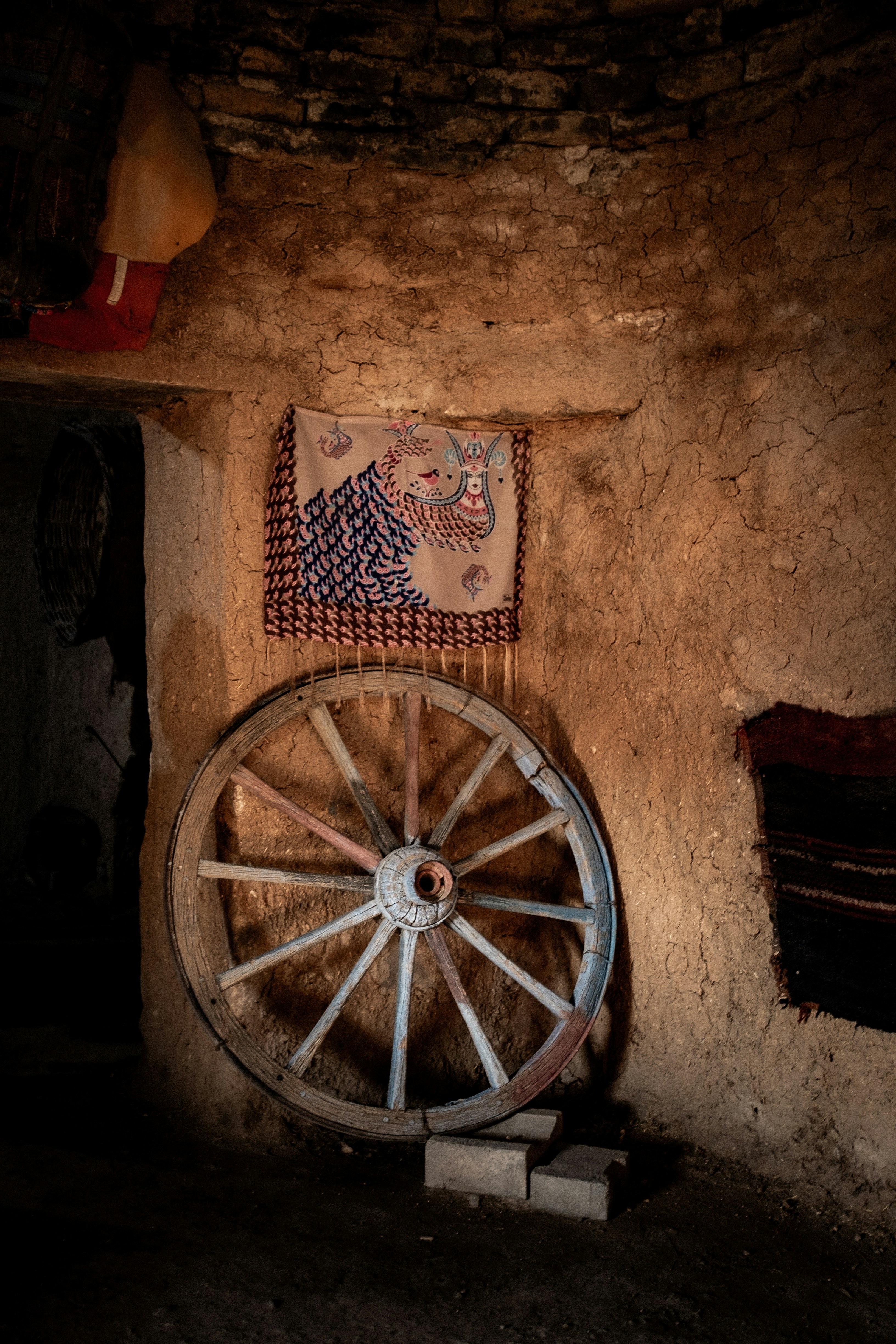 An old wooden wagon wheel leans against a textured wall.