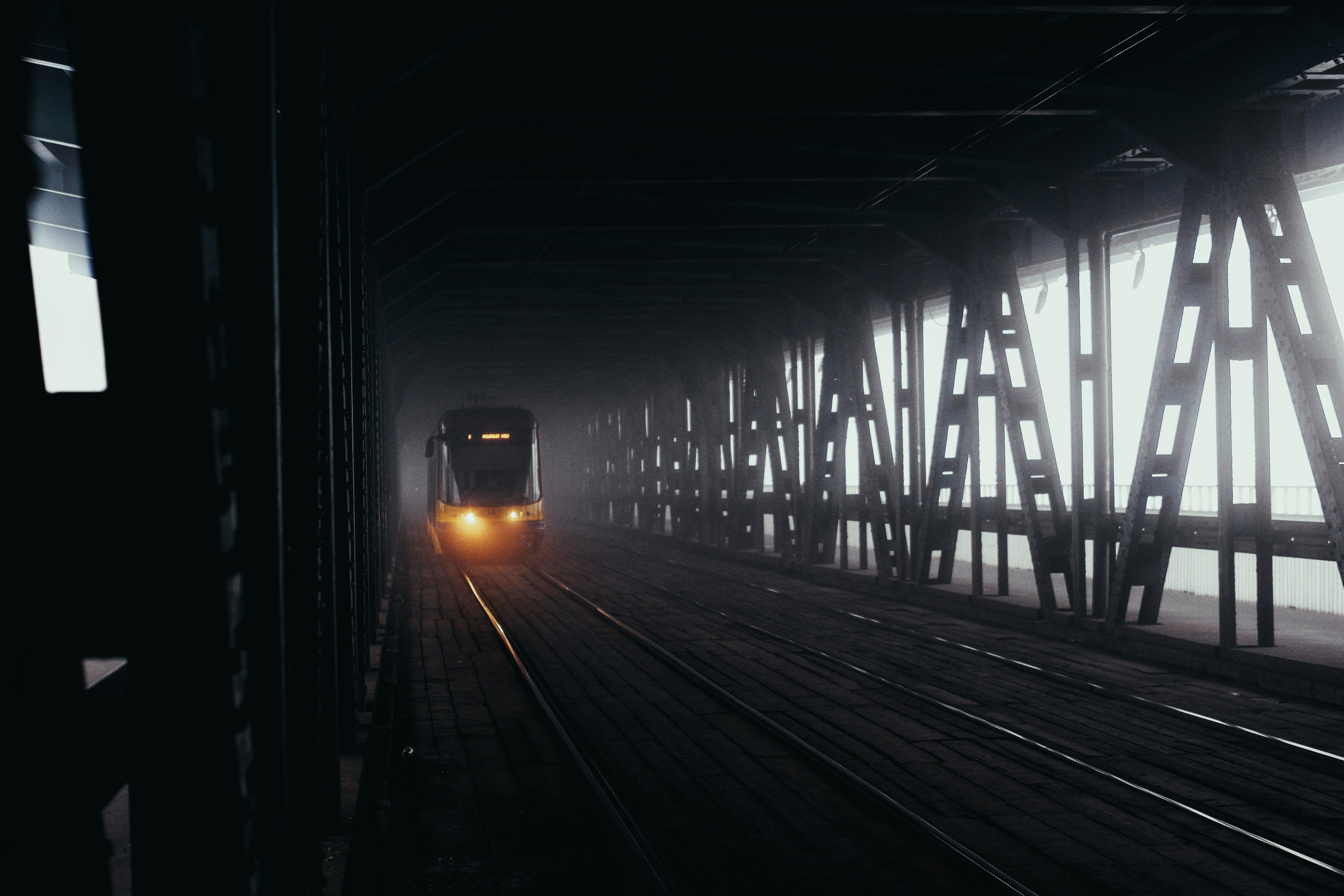 A train approaches through a foggy industrial bridge.