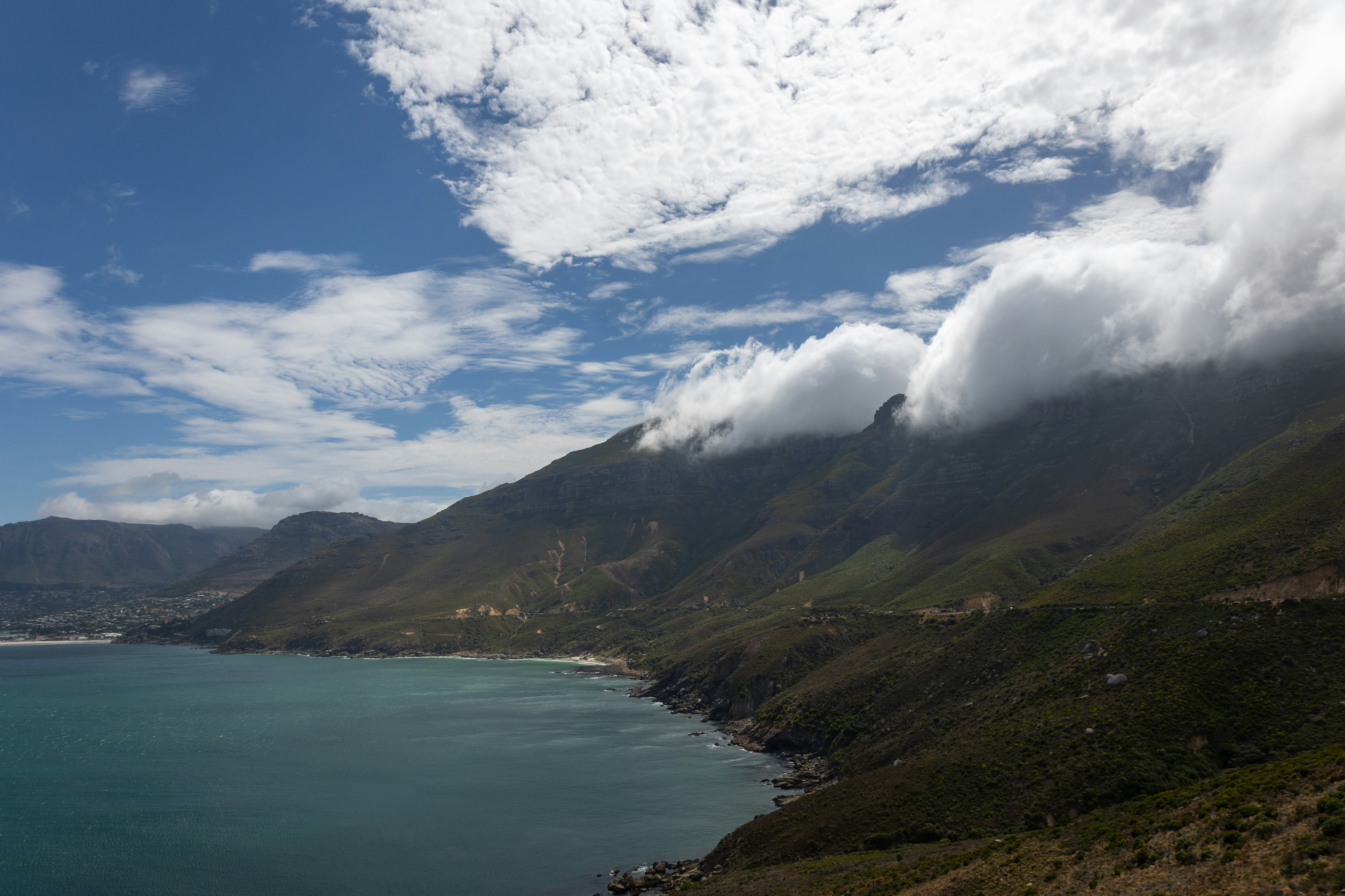 Coastal mountains meeting the turquoise ocean under clouds.