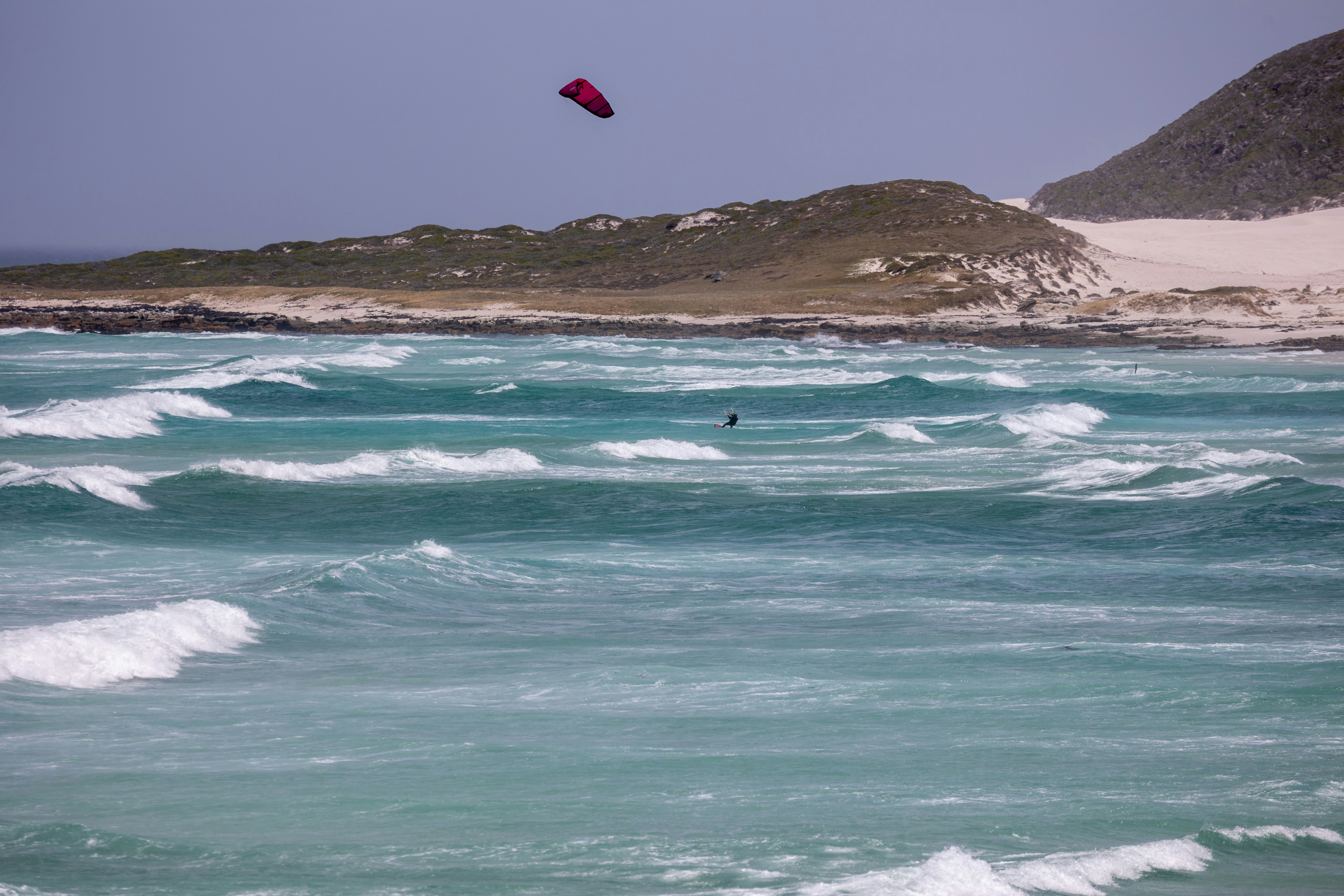 Kiteboarder in choppy turquoise ocean near sandy shore