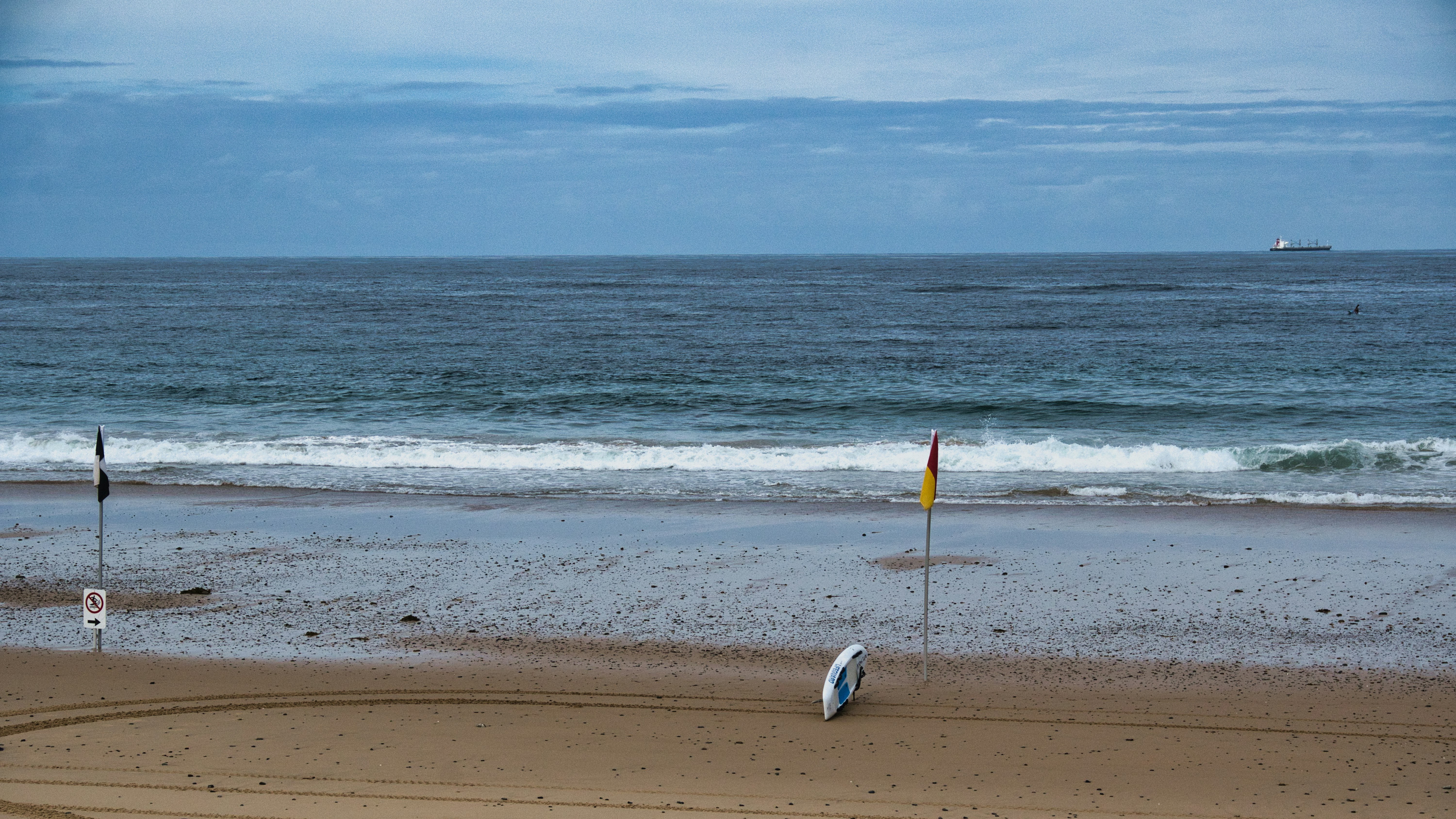 A deserted beach with flags and a surfboard